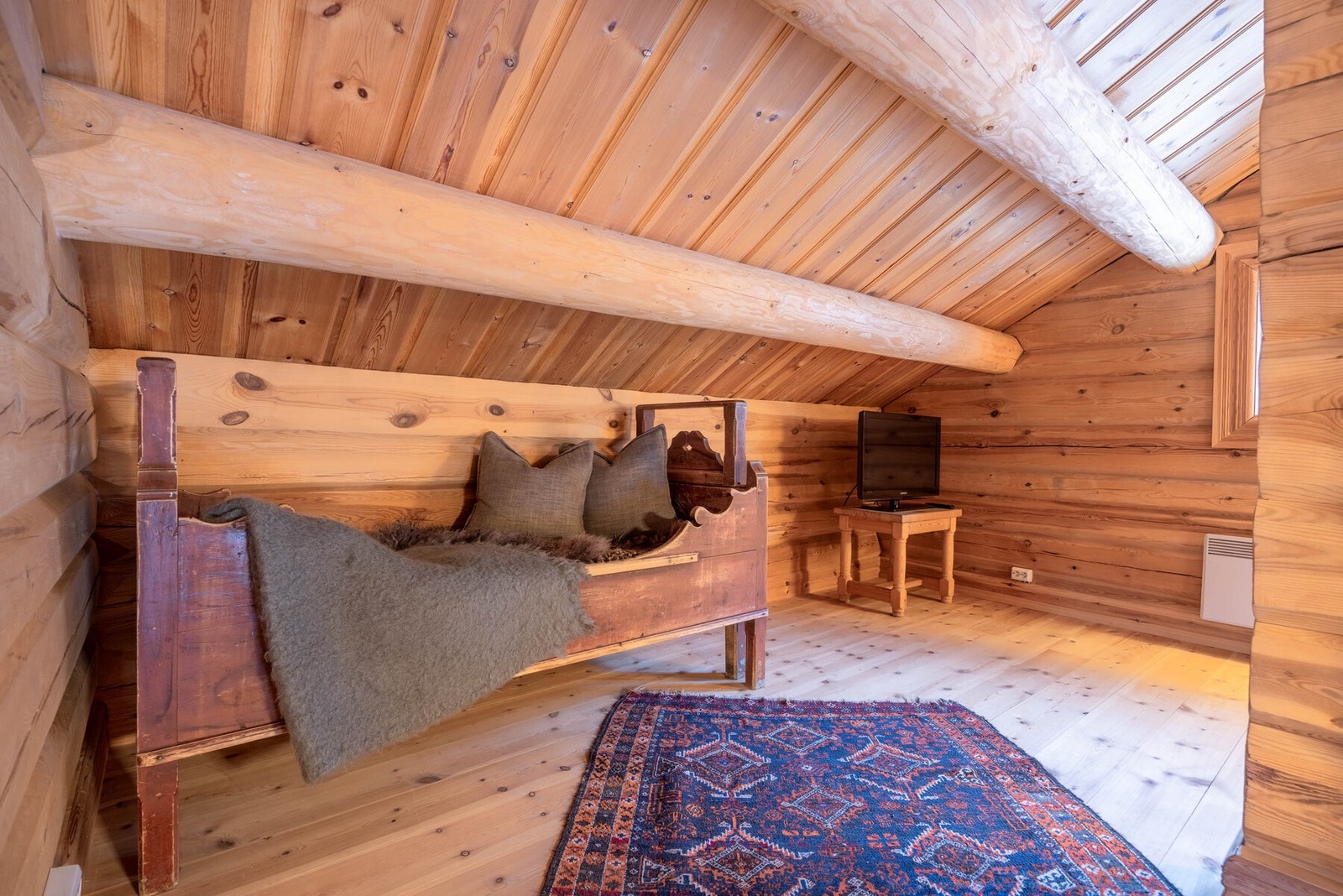 Loftstuen er et varmt og innbydende rom, der skråtaket og de synlige treflatene skaper en intim og rolig stemning. Galleribilde