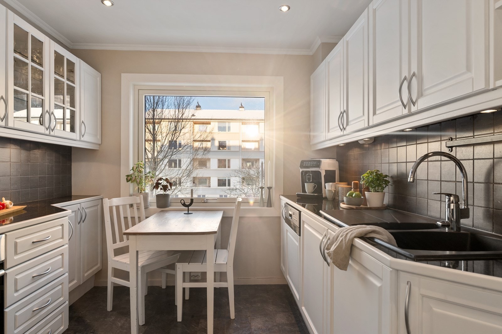 Kjøkkeninnredning med hvite profilerte fronter, laminat benkeplate med nedfelt vask og fliser på vegg over benk. Galleribilde