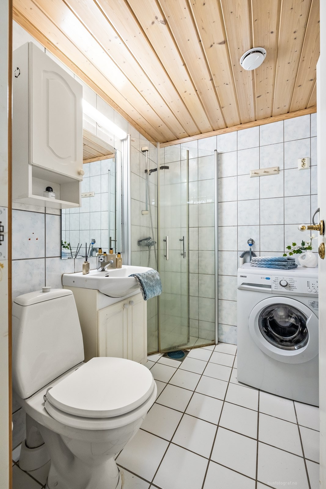 Badet er innredet med vegghengt servantinnredning med dører, speil med overlys, dusjhjørne med glassdører og gulvstående toalett Galleribilde