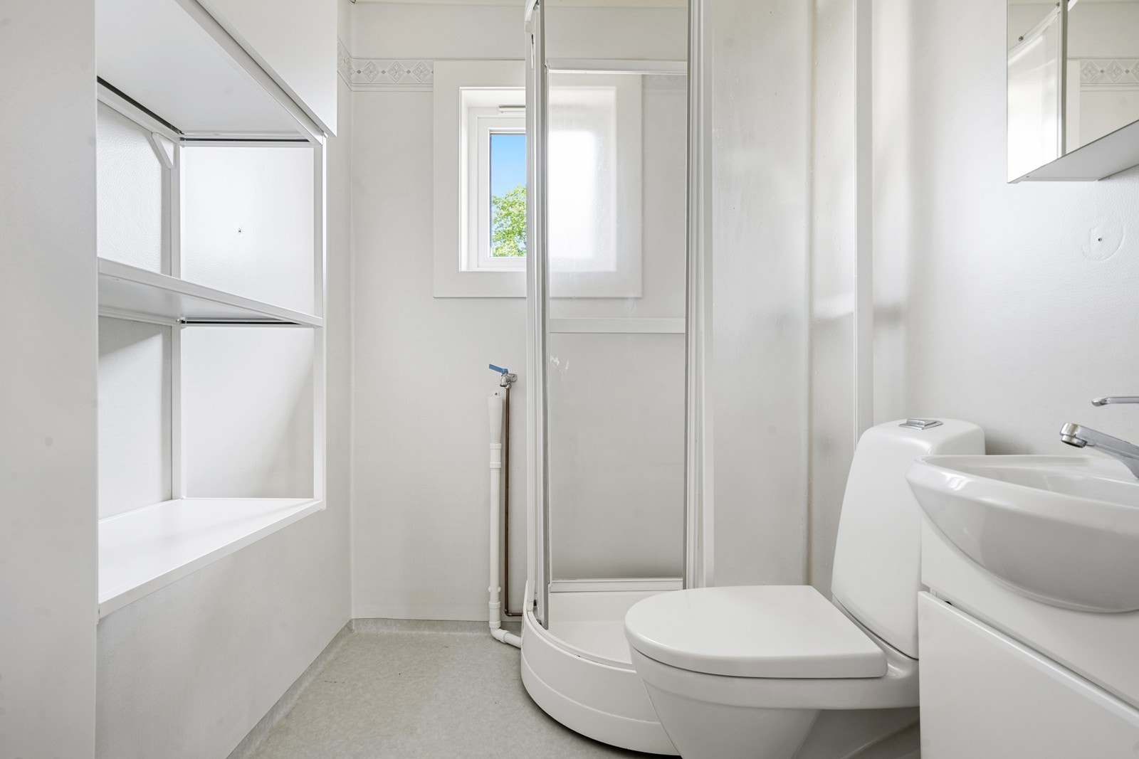 Baderommet er lyst og funksjonelt, med vinylbelegg på gulv og våtromstapet/belegg på vegger. Rommet er utstyrt med dusjkabinett, servant med skap og klosett. Det er også opplegg for vaskemaskin. Galleribilde