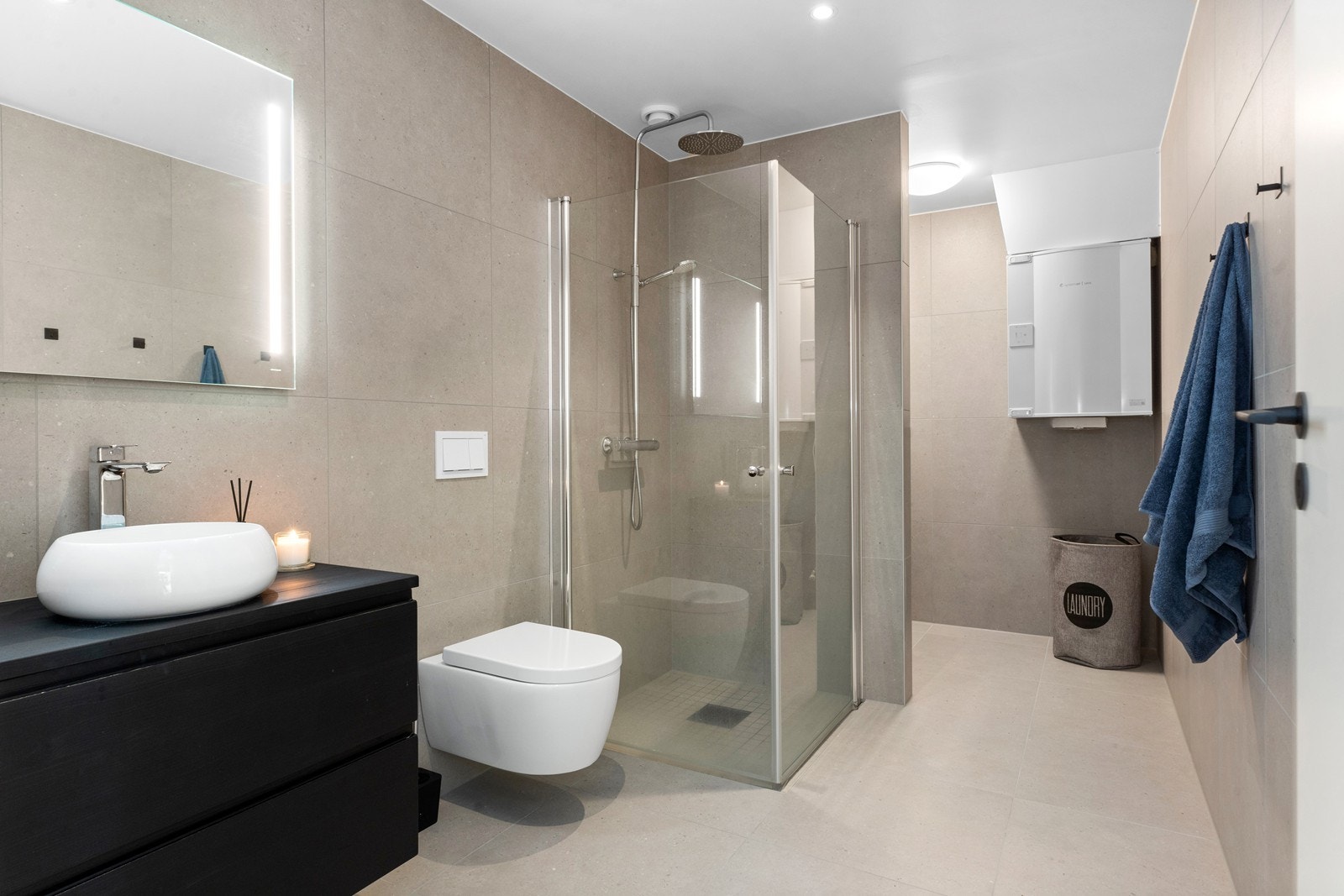 Baderomsinnredning i sort utførelse med speil på vegg. Det er dusjhjørne med glassvegger og vegghengt toalett. Galleribilde