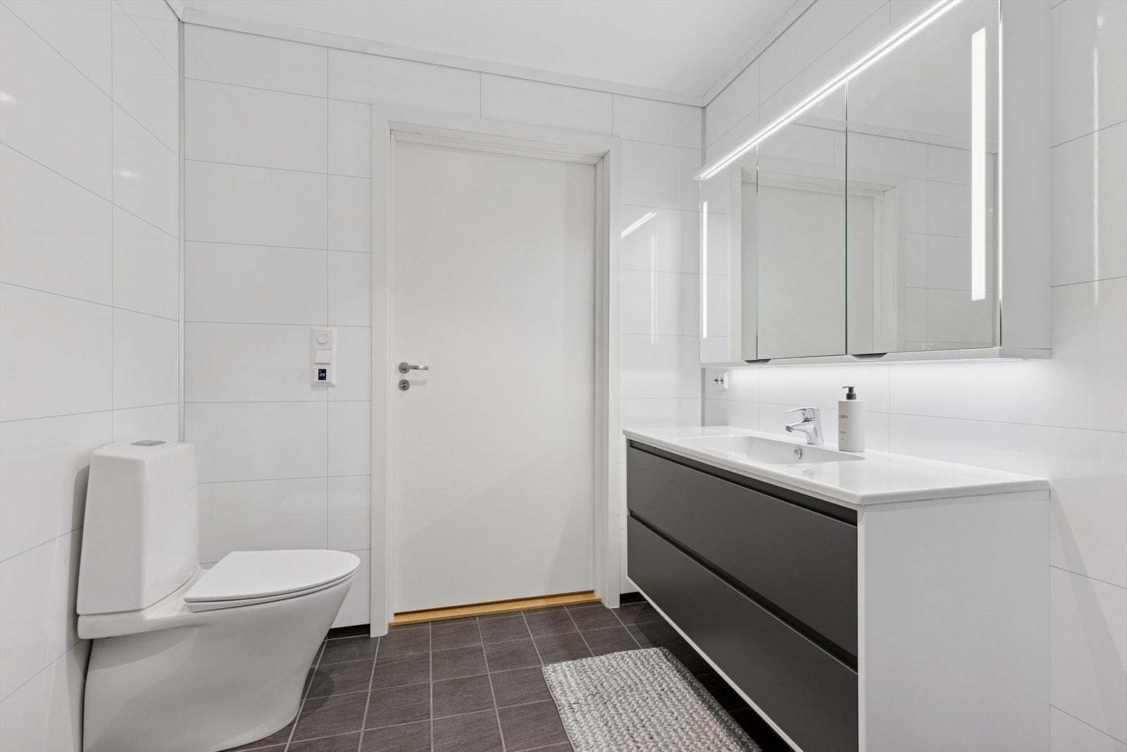 Badet er effektivt innredet med fliser på gulv. Innredning bestående av servant med skap og speil, wc samt dusj. Galleribilde