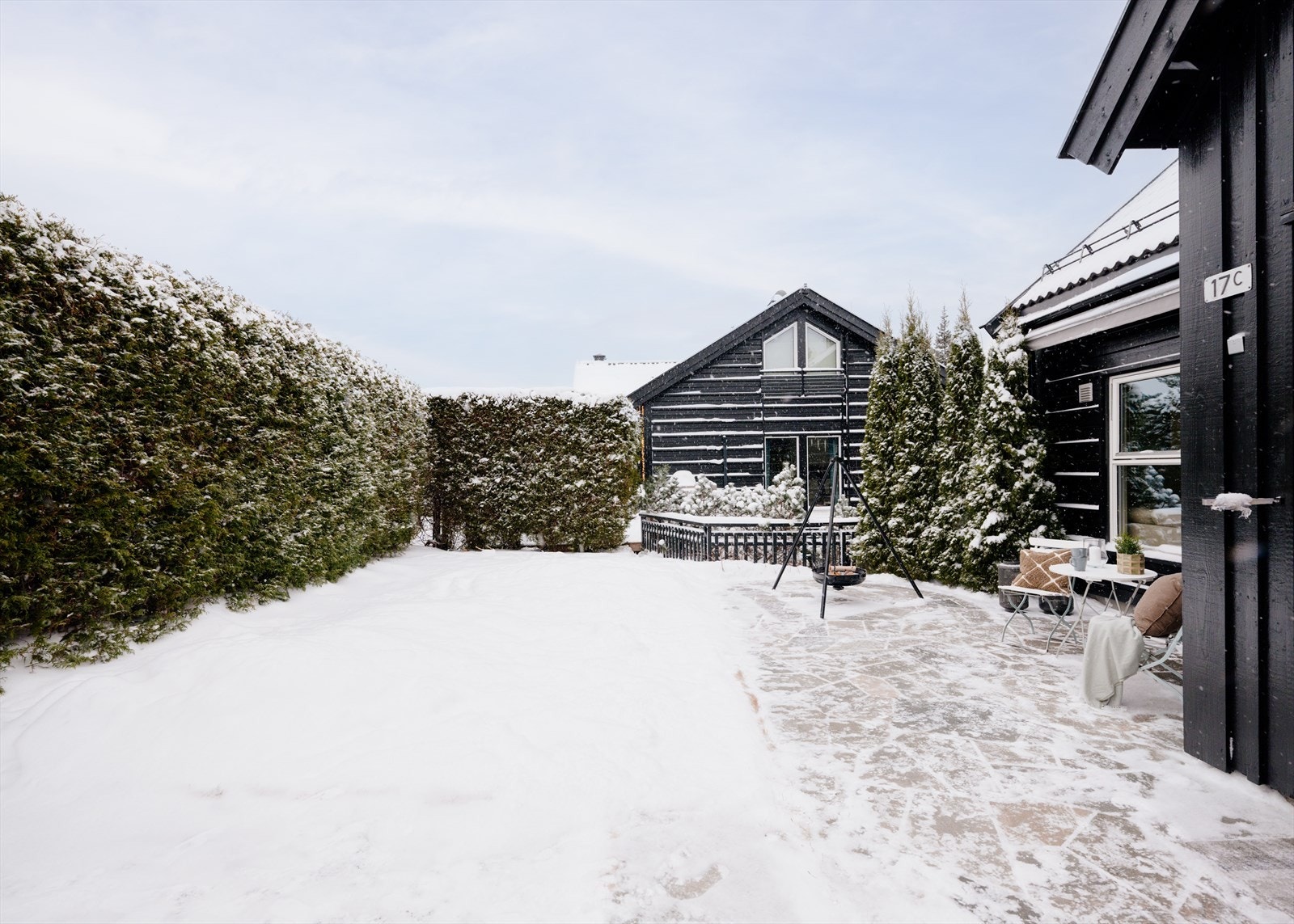 Steinlagt uteplass og hage på boligens vestside, skjermet med hekk. Et naturlig samlingspunkt sommer som vinter - perfekt for lek, avslapning og hyggelige måltider ute Galleribilde