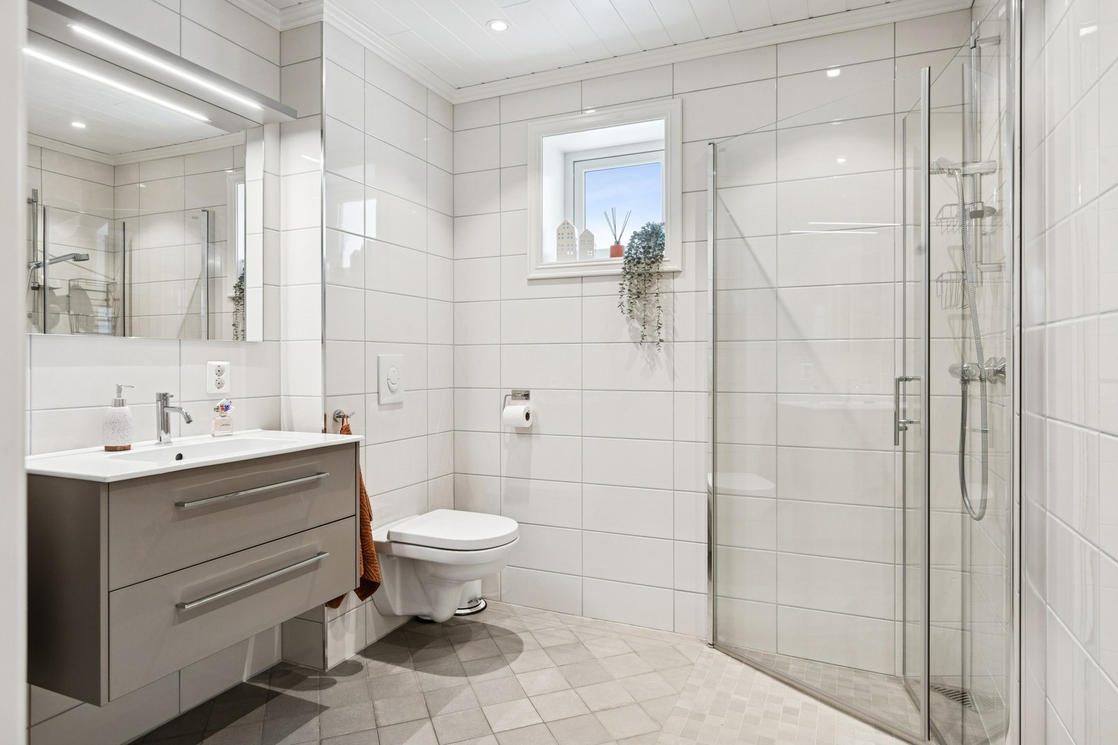 Bad med servant i skuffeseksjon, dusjløsning og vegghengt toalett. Galleribilde