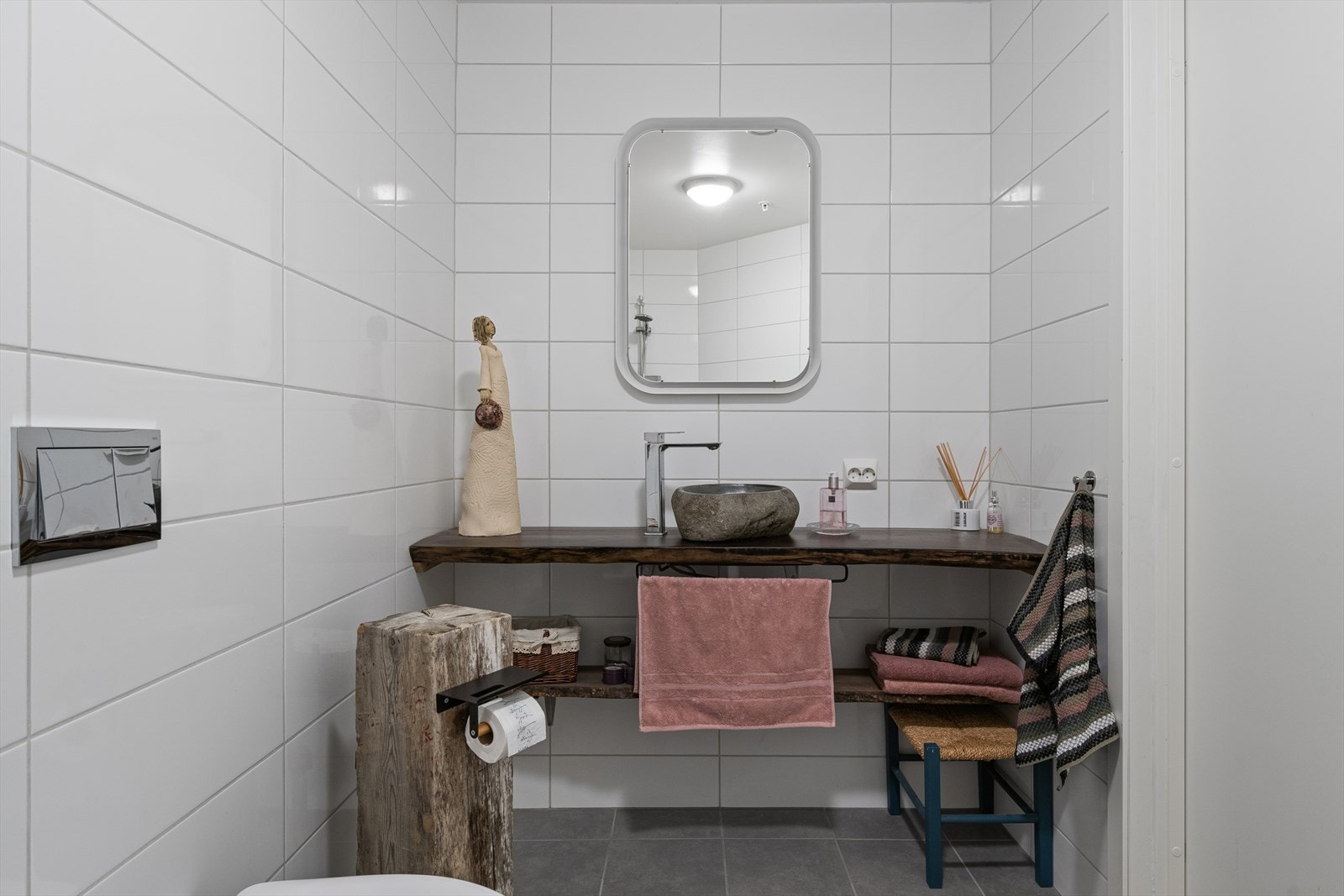 Badet har åpen dusj, vegghengt toalett og stedsbygd baderomsmøbel. Fliser på gulv- og veggflater i nøytale og tidløse farger. Galleribilde