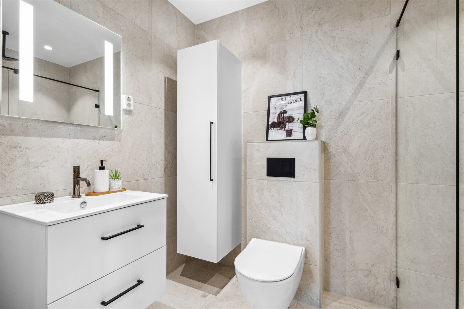 Badet i 3. etg. med fliser på vegg og gulv i lyse og fine toner. Badet er utstyrt med vegghengt toalett, innredning, høyskap, varmekabel og speil med lys. Galleribilde