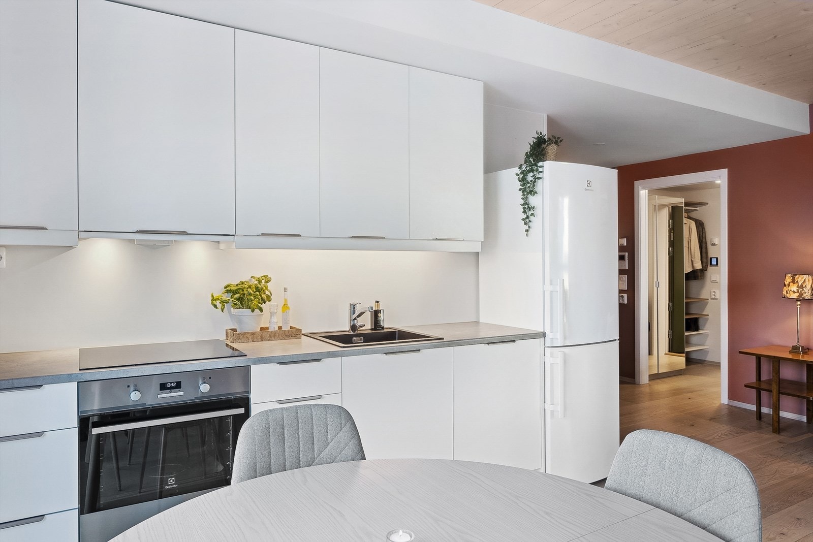 Kjøkken i åpen løsning mot stuen. Moderne innredning i hvit, glatt utførelse, og med integrerte hvitevarer. Galleribilde