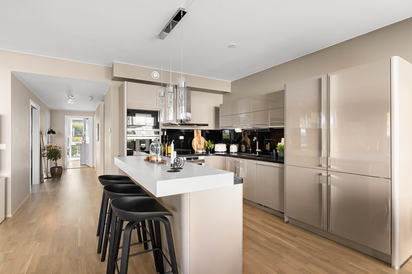 Høyglansede fronter og avrundede hjørner gjør den omfangsrike kjøkkeninnredningen lite fremtredende i rommet. Galleribilde