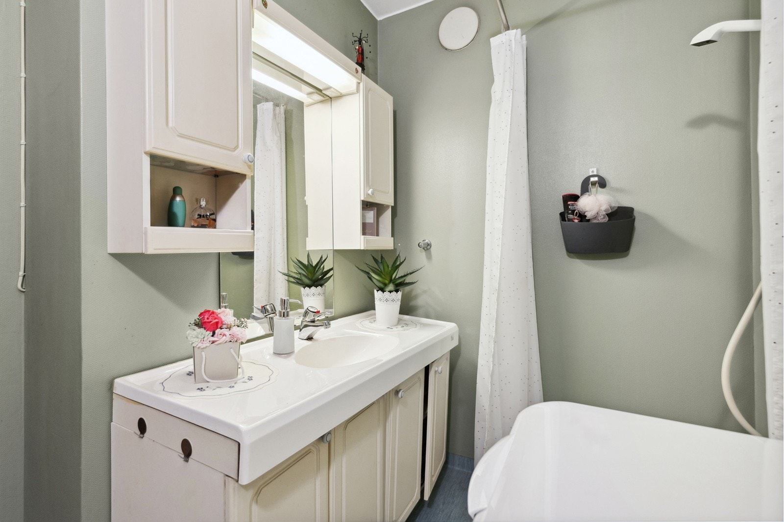 Badet er fra byggeåret og har malt tapet på veggene og vinylbelegg på gulvet. Innredningen består av servant med underskap, sideskap og speil, samt frittstående toalett og dusjhjørne. Galleribilde