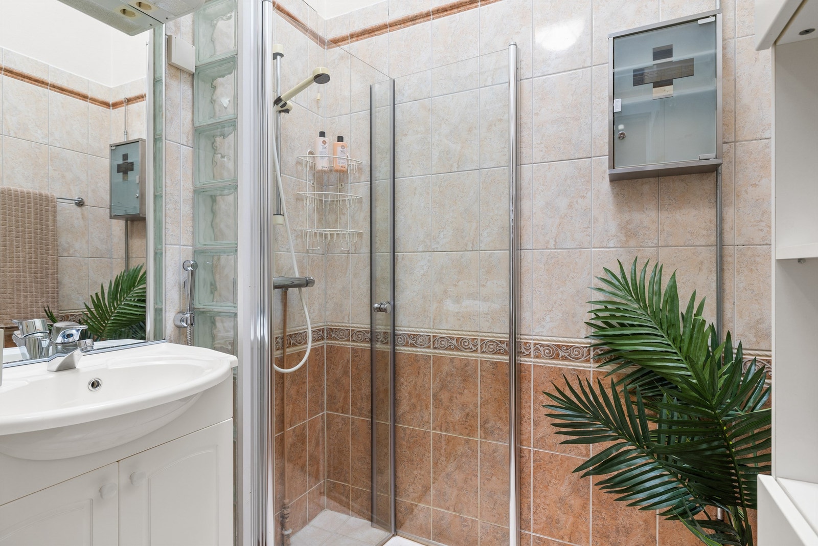 Baderom med flislagt vegger og gulv med varme. Det er utrustet med vegghengt servantskap med profilerte fronter og nedsenket servant. Vegghengt speil med overbelysning. Dusjhjørne med innfellbare glassdører. Galleribilde