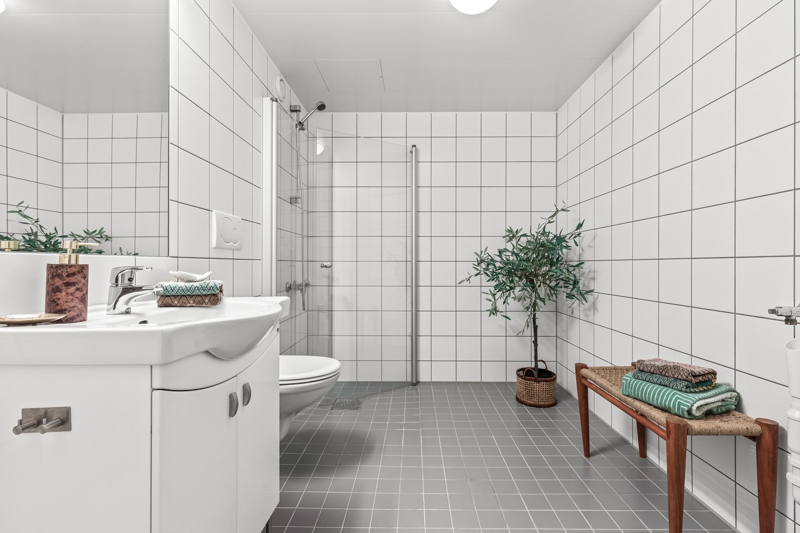 Romslig og flislagt bad med tidløst uttrykk og praktisk planløsning. Galleribilde