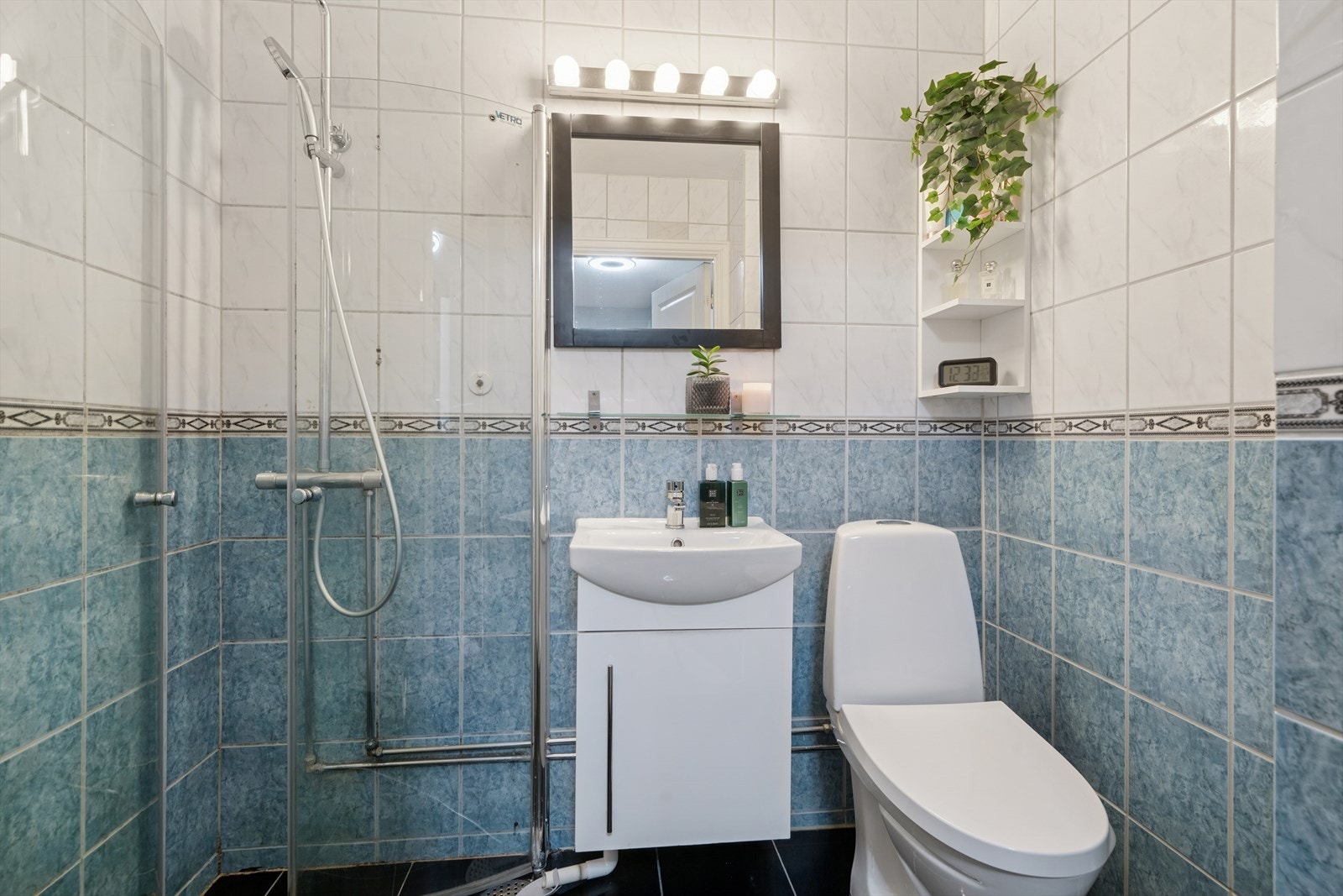 Baderommet inneholder dusjhjørne, servant med underskap, speil med belysning og toalett. Galleribilde