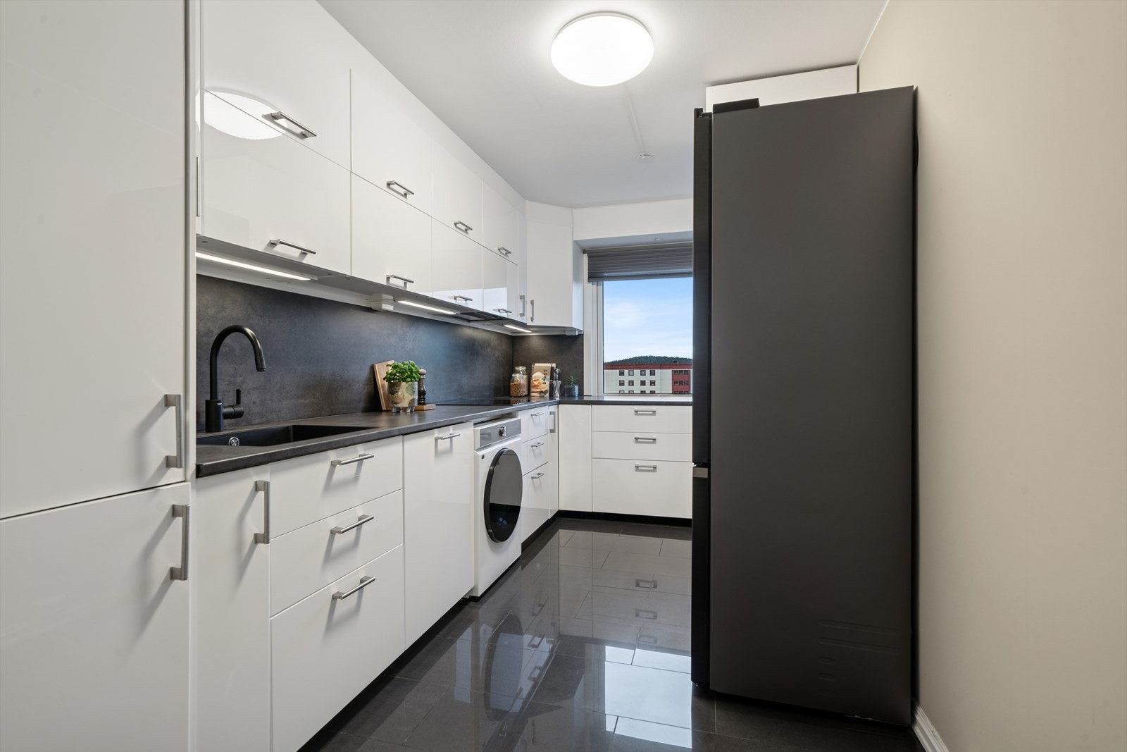 Hvite, glatte fronter kombinert med store vindusflater skaper et luftig og innbydende kjøkkenmiljø. Galleribilde