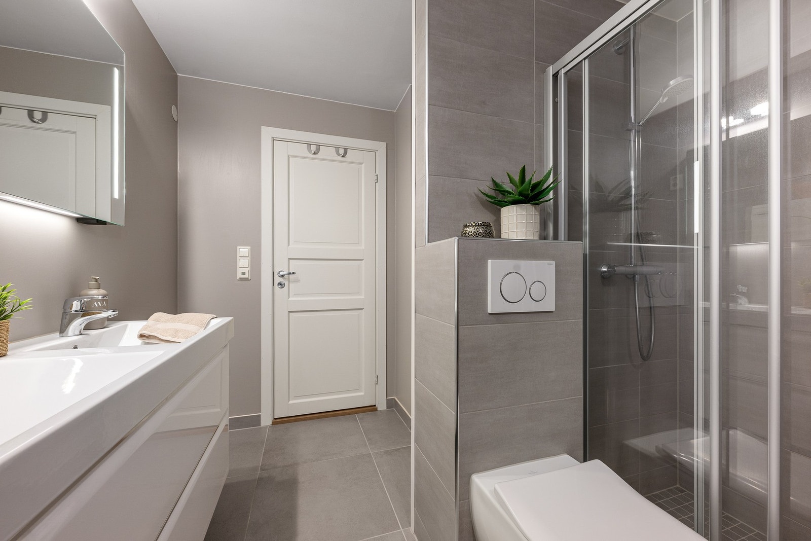 Flislagt baderom fra 2017 med gjennomtenkt planløsning, dobbel servant, veggmontert toalett, dusjhjørne med skyvedør og opplegg for vaskemaskin og tørketrommel. Galleribilde