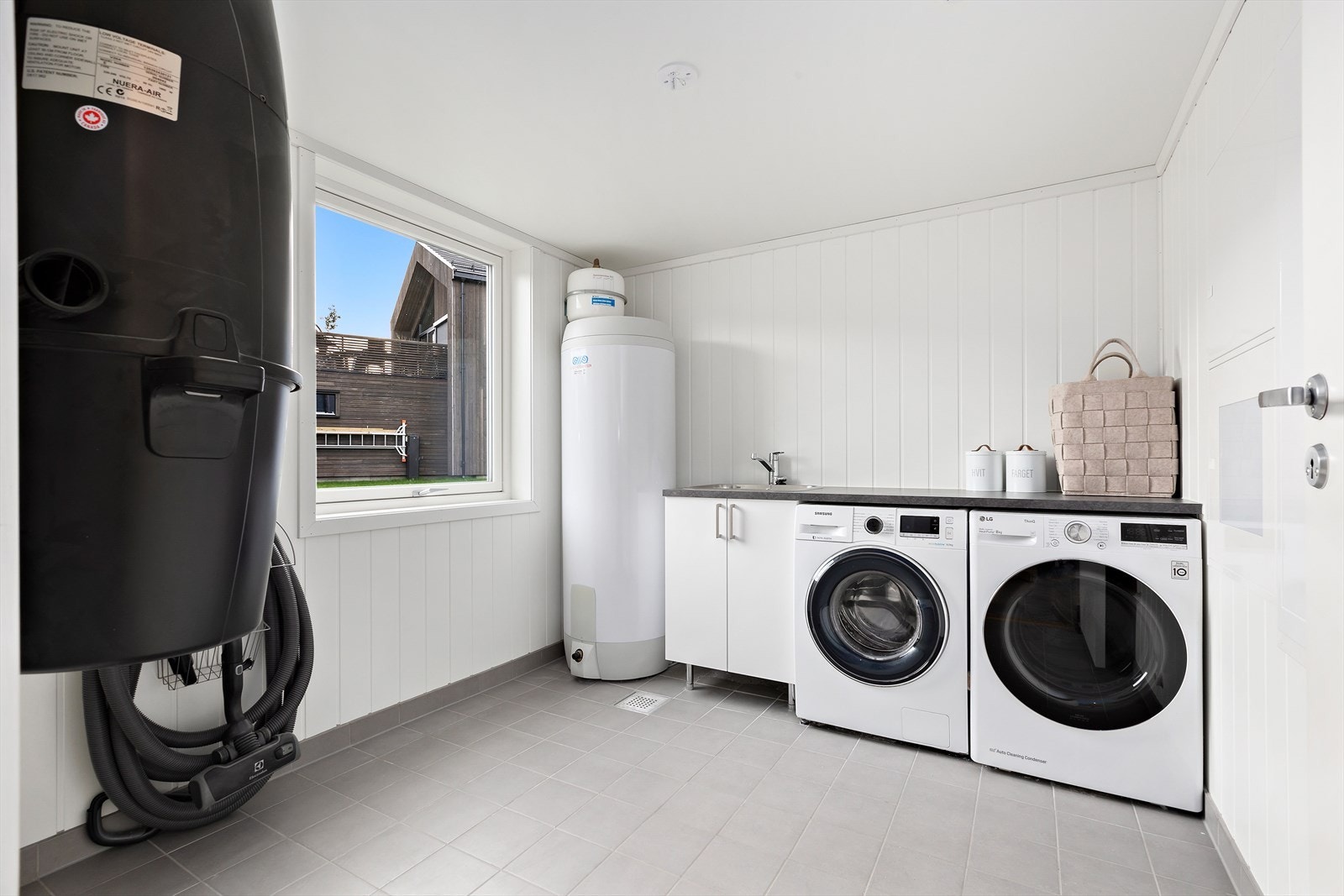 Praktisk vaskerom med plass til diverse oppbevaring. Rommet har benkeplate med skylle kum og det er opplegg for vaskemaskin og tørketrommel. Galleribilde