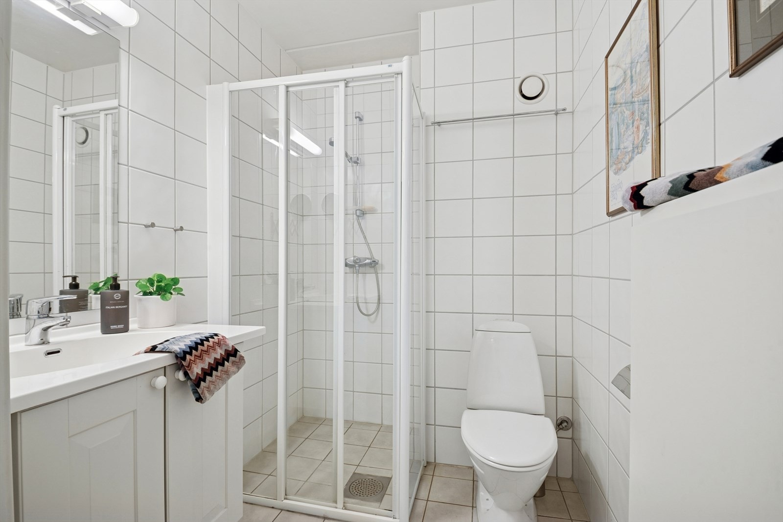 Flislagt bad med varmekabel. Badet er utstyrt med servant med servantskap, toalett og hjørnedusj med glassdører/vegger med fast gulvskinne. Galleribilde