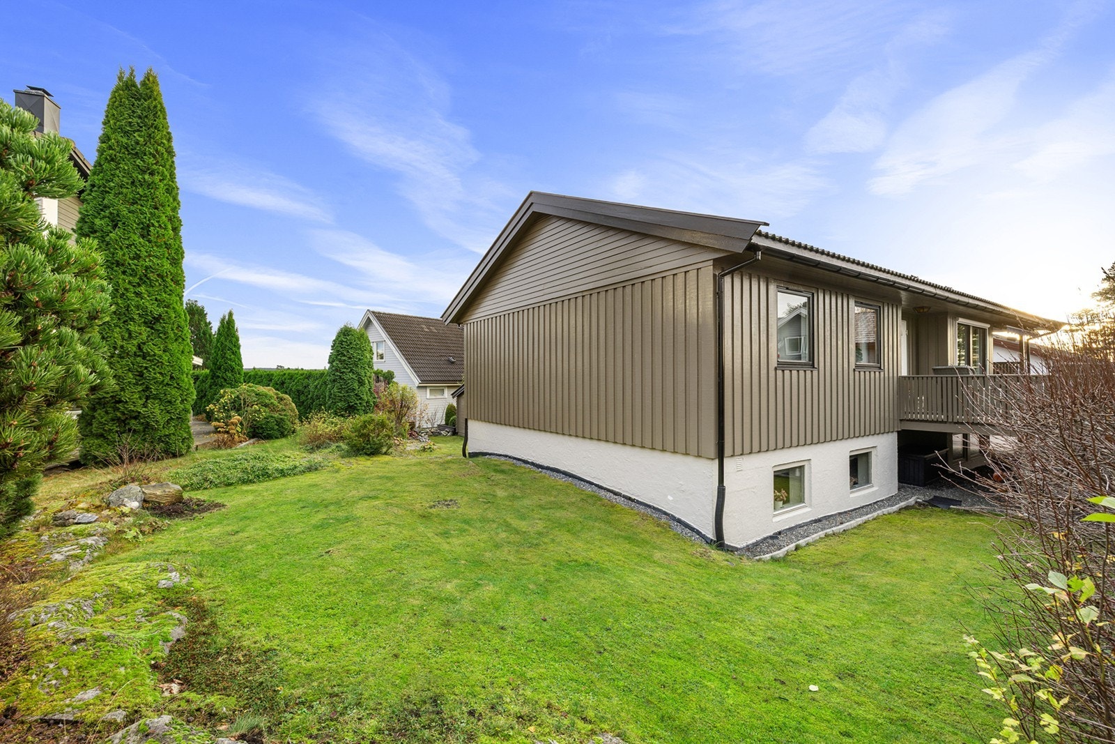 Velstelt og solrik hage som omkranser boligen, med plen, prydbusker og grønne hekkplanter som gir en skjermet og trivelig atmosfære. Galleribilde