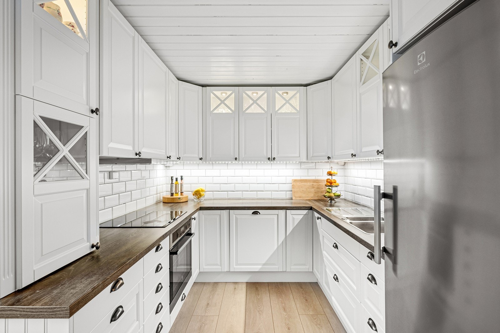 Kjøkken med klassisk hvit innredning og god utnyttelse av plassen. De mange skapene gir rikelig oppbevaringsplass, og de lyse overflatene sammen med underbelysning skaper en trivelig atmosfære. Galleribilde