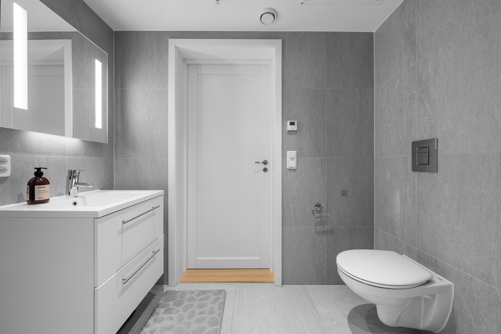 Badet er innredet med dusjhjørne med foldbare glassdører, vegghengt wc, servantskap med skuffer og speil med integrert belysning Galleribilde