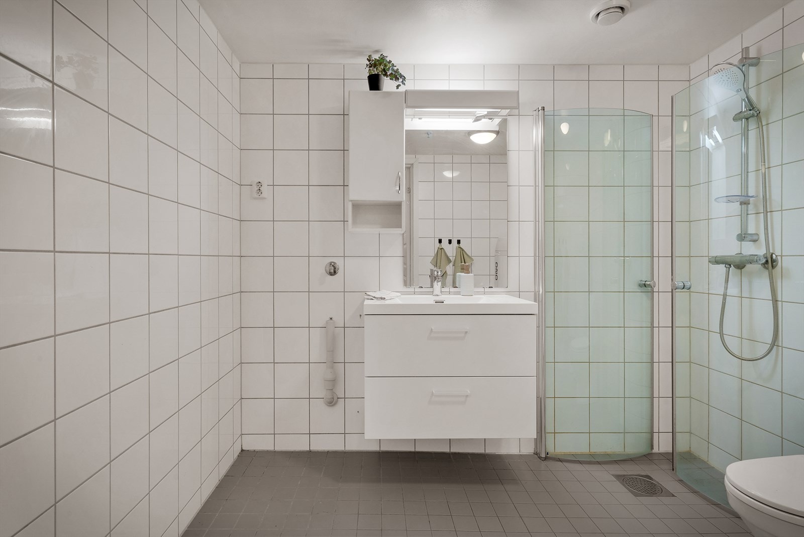 - Badet er innredet med benkeskap med servant, dusjdører, gulvmontert toalett og opplegg for vaskemaskin - Galleribilde