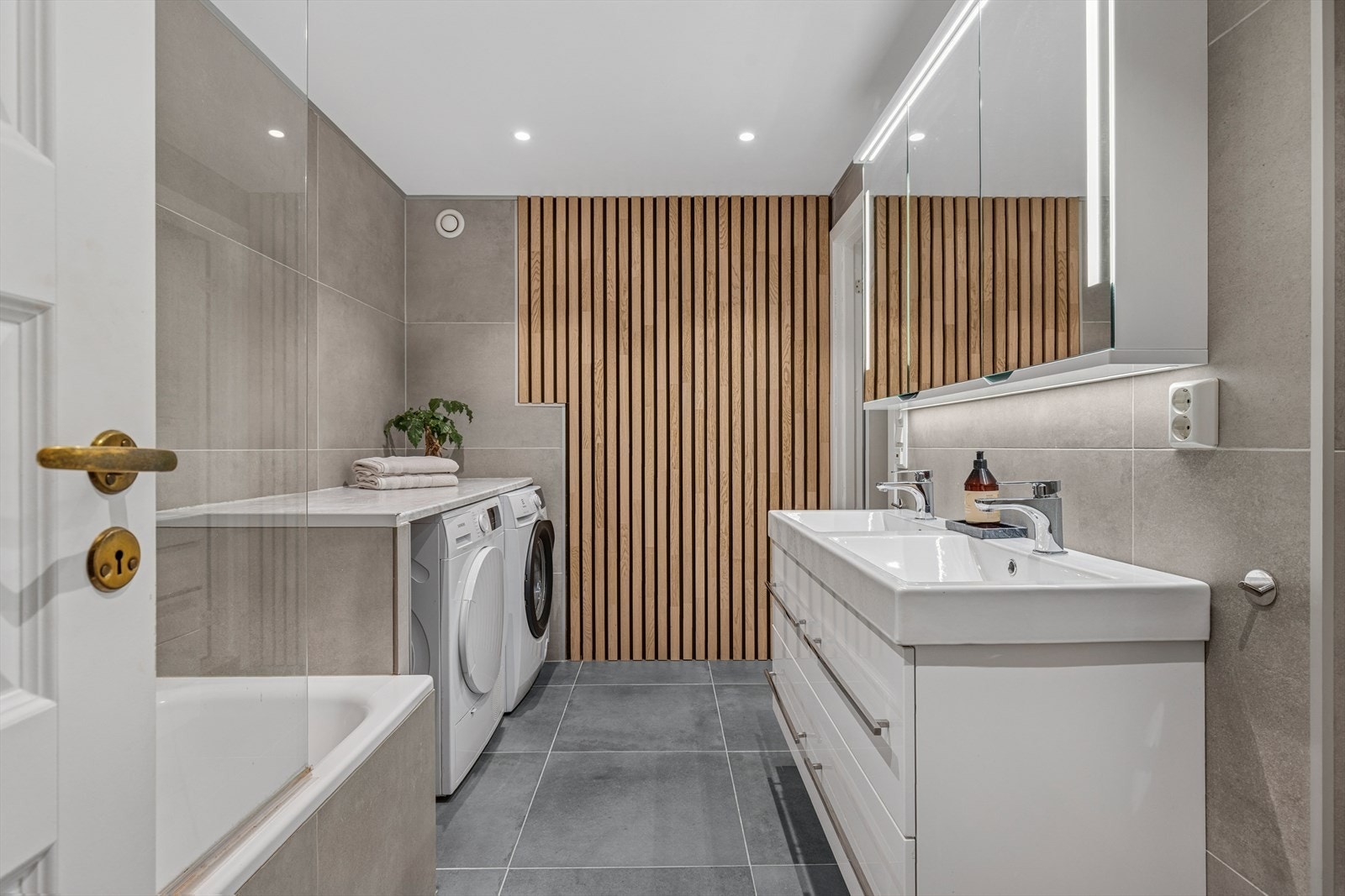 Badet ble pusset opp i 2018 og er innredet med store, grå fliser på gulv og vegger og varmekabler i gulvet for ekstra komfort. Spileveggen er en lettvegg mellom badet og toalettrommet og skaper en flott kontrast til de grå flisene. Galleribilde