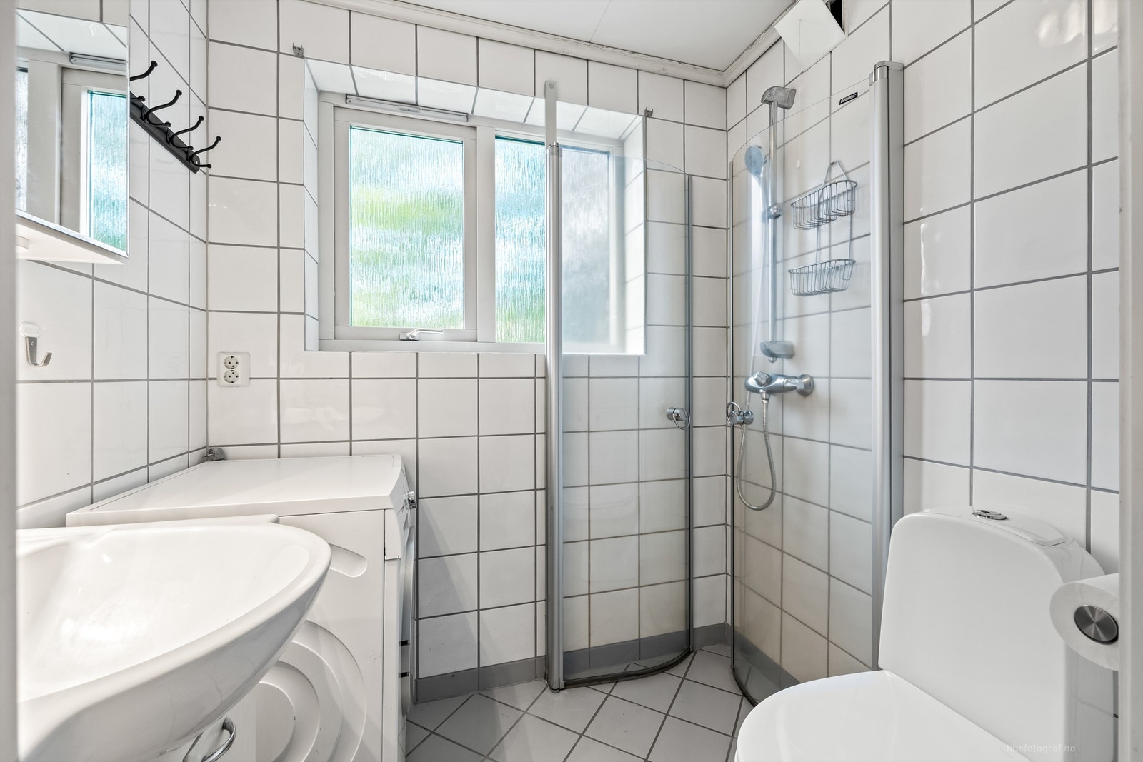 Innredet med vegghengt servantinnredning med slette dørfronter, speilskap over servant, gulvstående toalett, dusjhjørne og opplegg for vaskemaskin Galleribilde