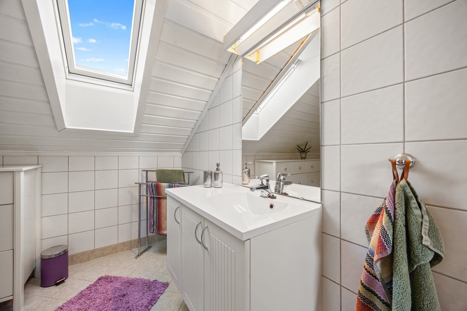 Flislagt bad fra byggeår med varme i gulvet for ekstra komfort. Her finner du dusj på gulv, gulvstående toalett, servant med underskap og speil. Galleribilde