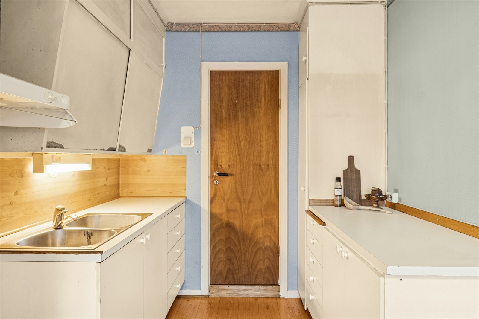 Kjøkkenet har en eldre innredning med laminerte og malte skrog, slette fronter og en laminert benkeplate med nedfelt oppvaskkum i stål. Galleribilde