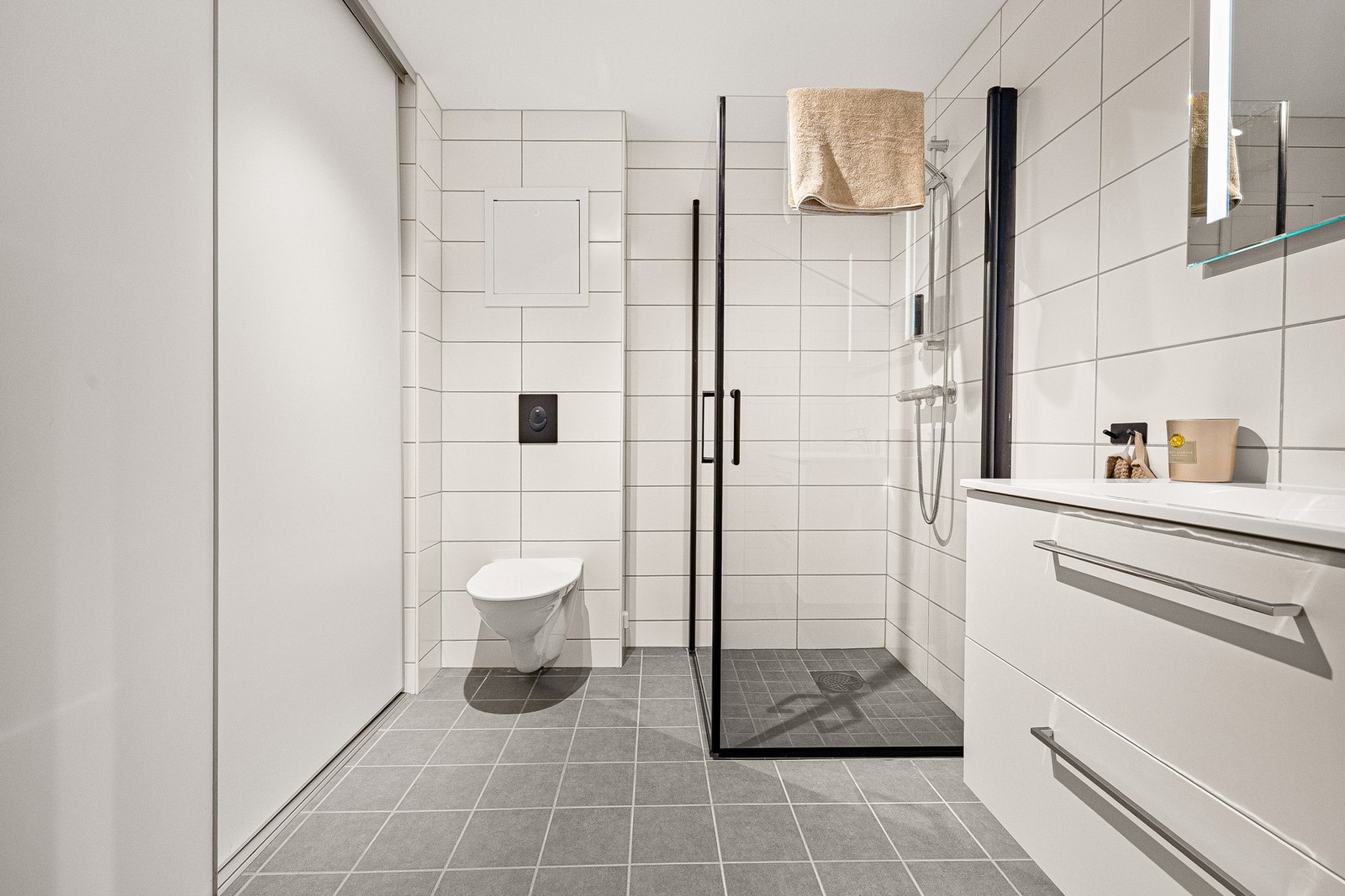 Rommet er innredet med innredning med servant og skuffer, speil med lys, dusjnisje med hengslede glassdører og nedsenket dusjsone, samt vegghengt toalett. Galleribilde