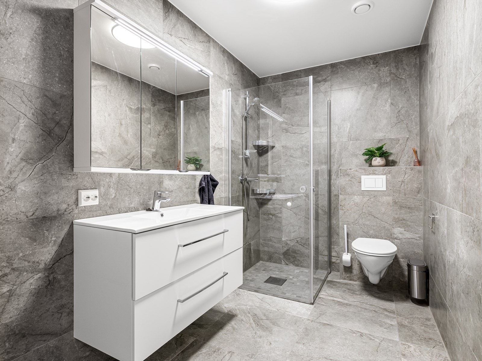 Lekkert helfliset bad med vegghengt wc, vask i seksjon og speil med belysning. Dusj med fleksible glassdører. Varmekabler i gulv. Galleribilde