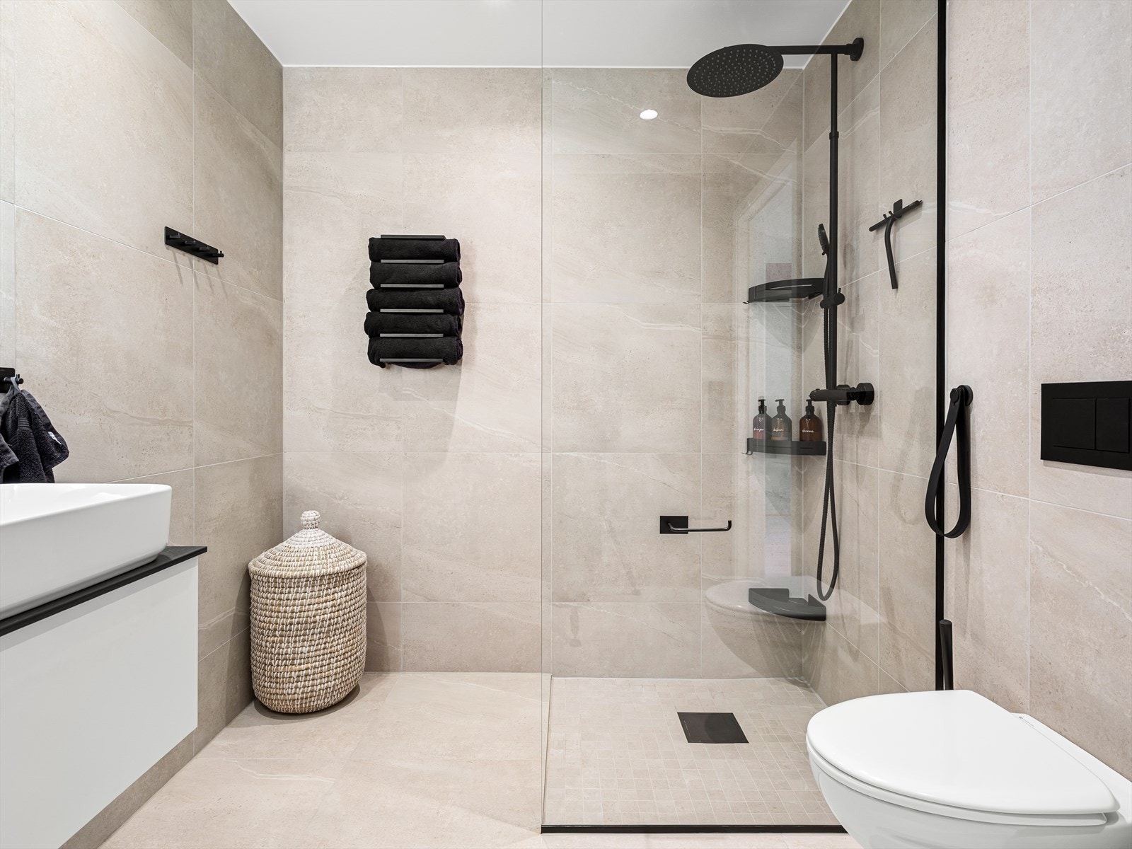 Pent bad med fliser på gulv og vegg. Vegghengt wc, vask i skuffeseksjon, og dusj med stilfull glassvegg. Galleribilde