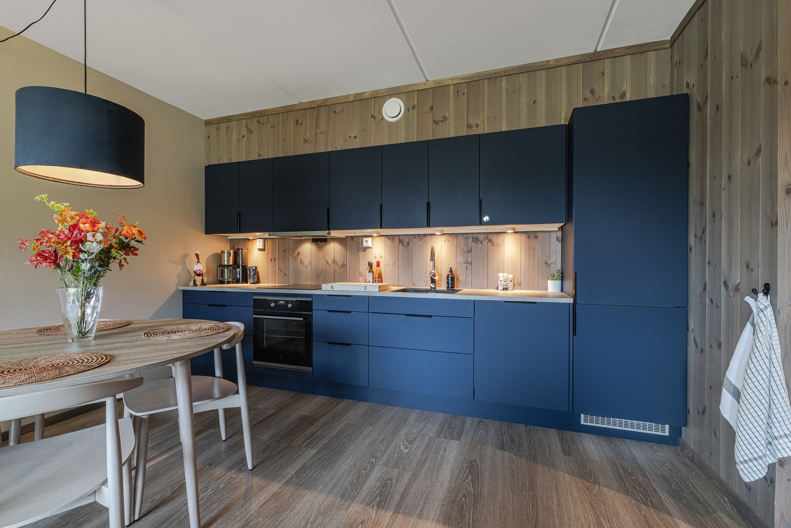 Moderne kjøkken med stilrene blå skapfronter og trepanel på veggene, gir en varm og innbydende atmosfære. Galleribilde