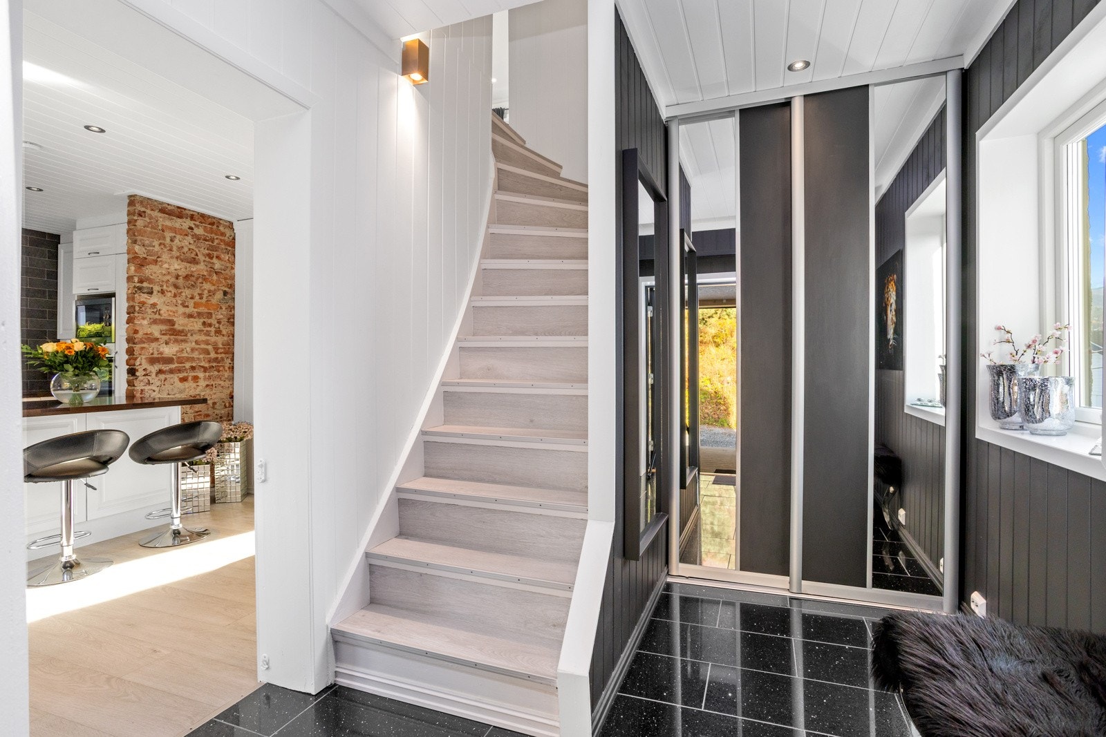 Flislagt gulv i entré og skyvedørsgarderobe med speil reflekterer lyset fra vinduet. Galleribilde