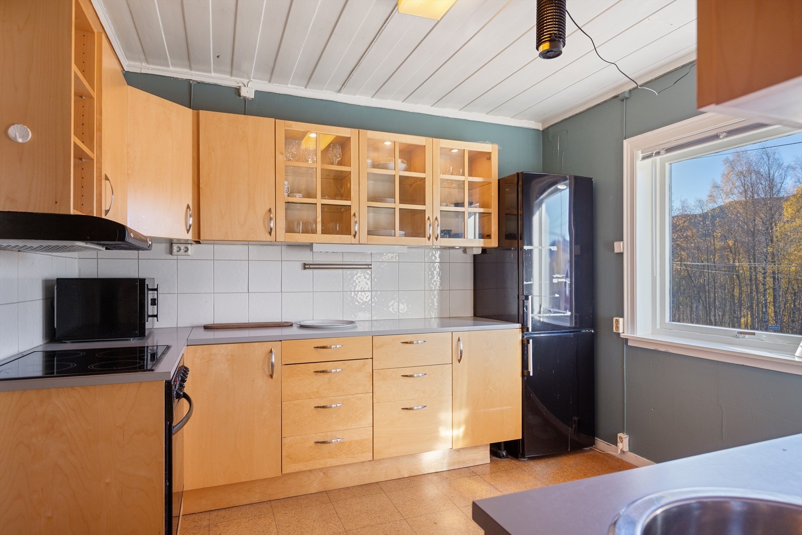 Innredningen har skap med både tette og glassfelte dører, laminert benkeplate og fliser mellom benk og overskap. Løsningen gir god arbeidsplass og fine lagringsmuligheter. Galleribilde