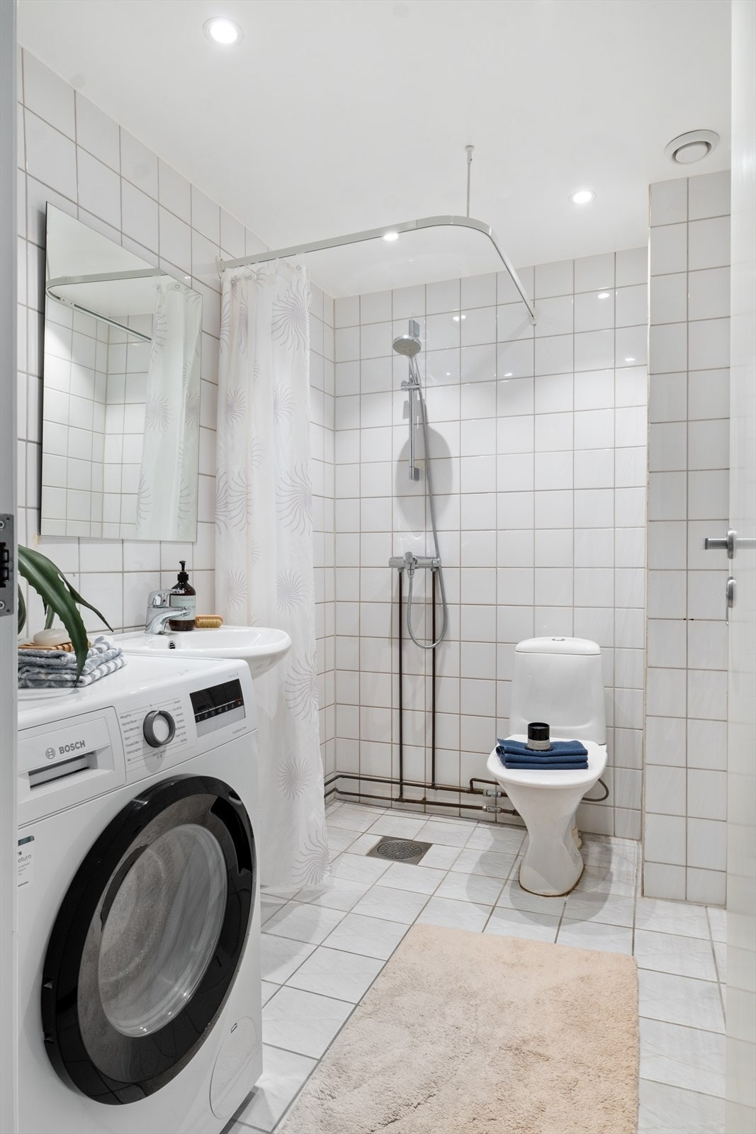 Flislagt baderom med panelovn, avtrekk, speil, downlights, opplegg for vaskemaskin, servant, dusj hjørne med forheng og toalett. Galleribilde