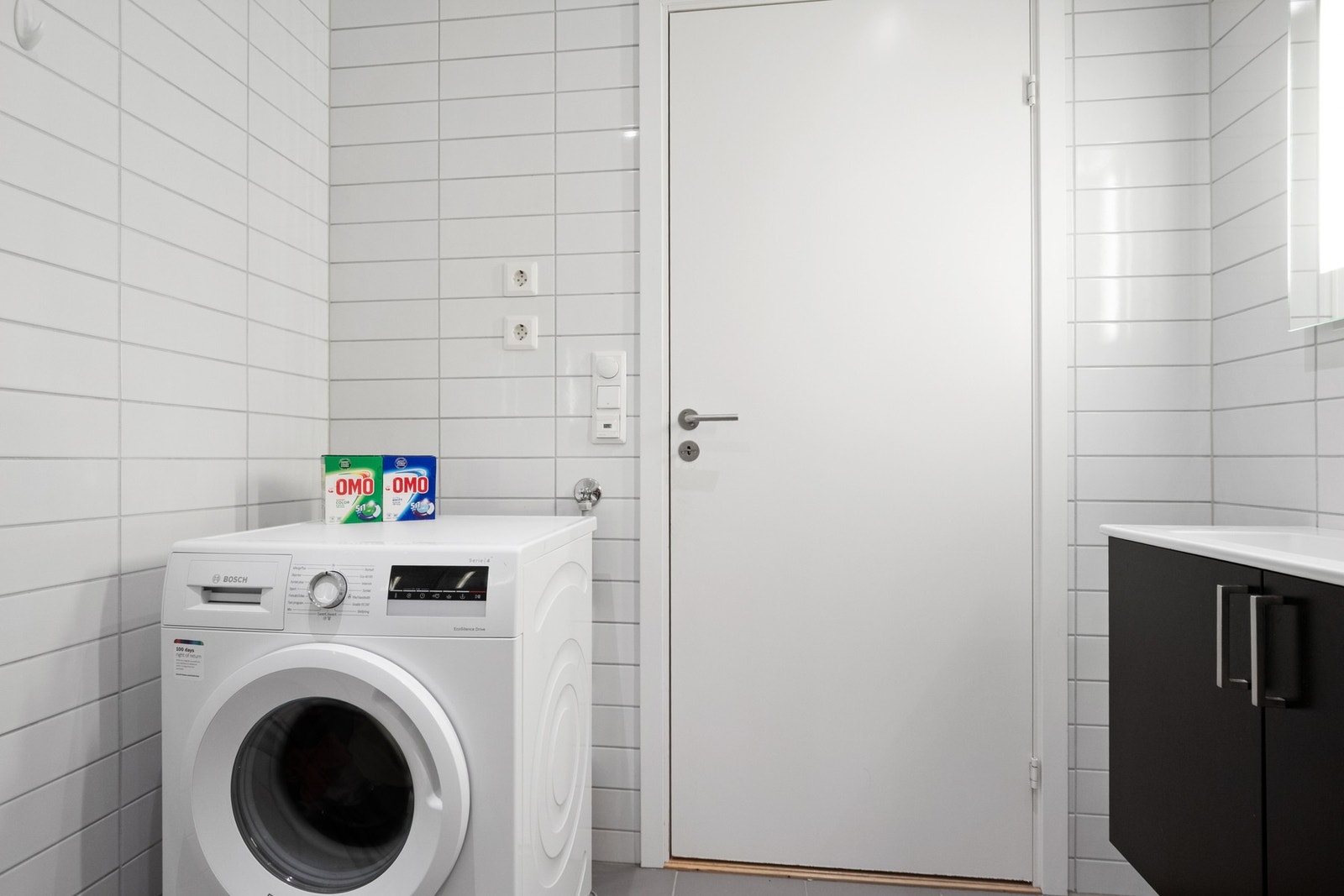 Videre er badet utstyrt med veggmontert toalett, dusjhjørne med innfellbare glassdører og opplegg for vaskemaskin Galleribilde