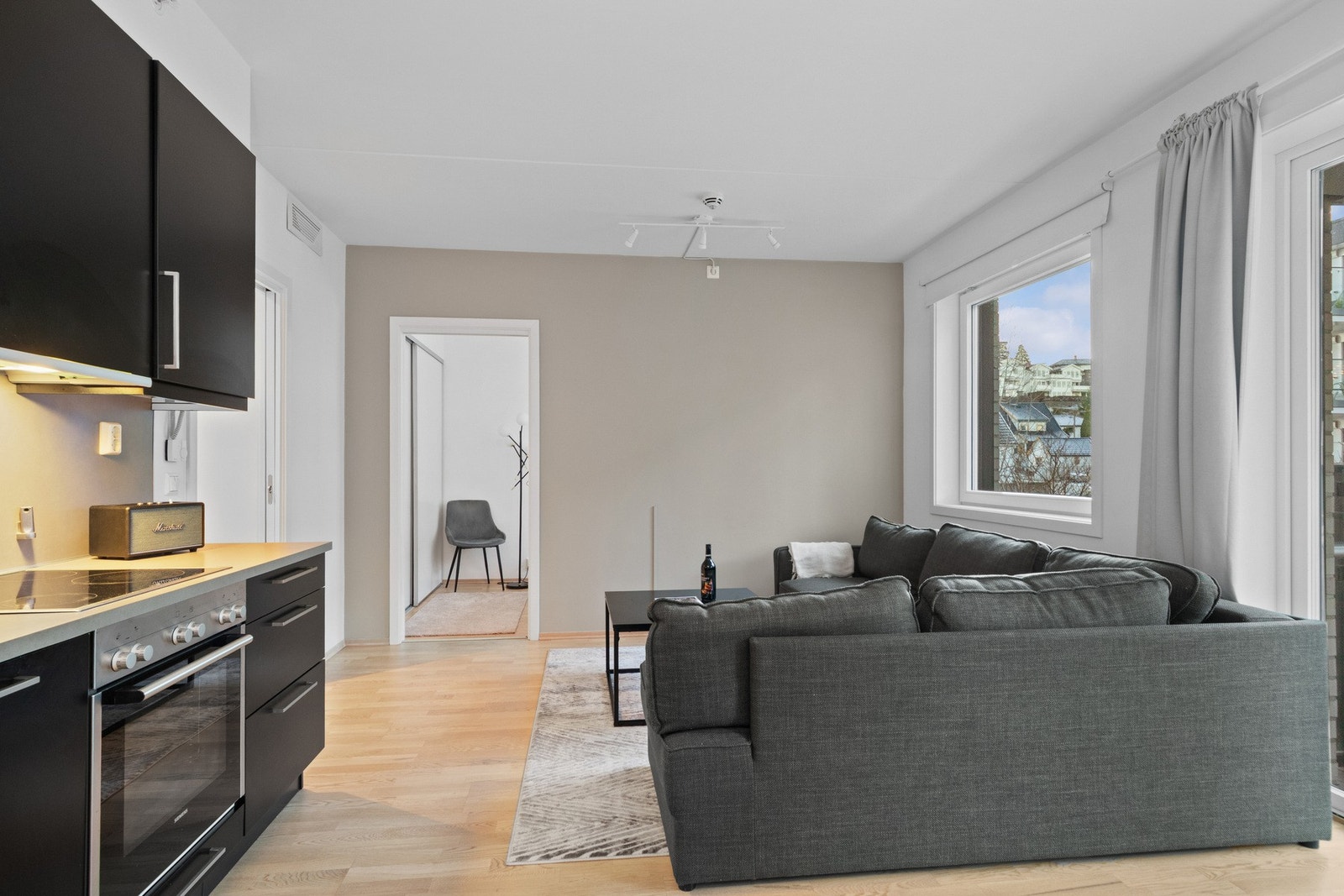 Stuen har gode vindusflater langs endeveggen for behagelig lysforhold og utgang til overbygd balkong med glassrekkverk Galleribilde