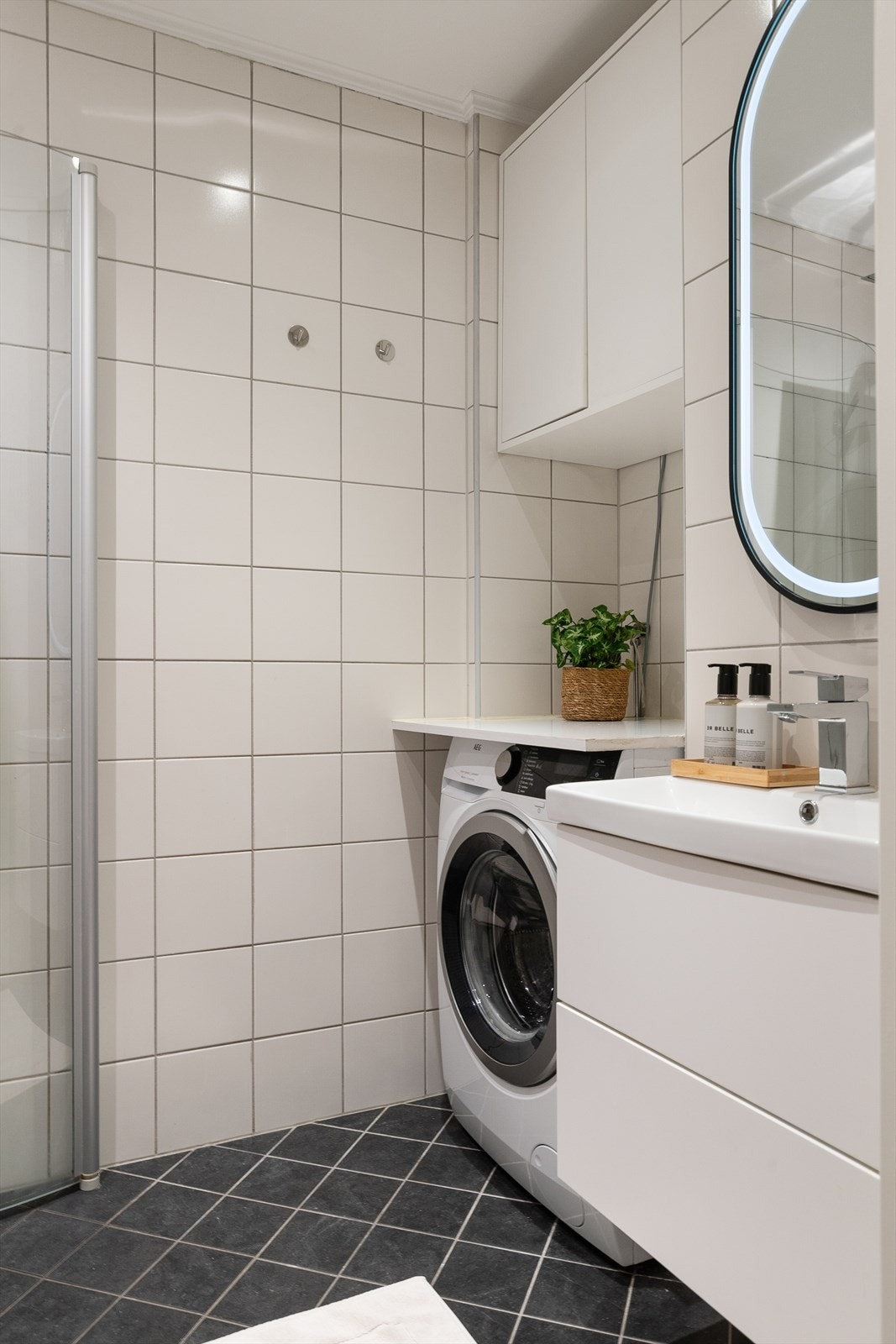 Videre er det veggmontert toalett og et dusjhjørne med innfellbare dusjvegger, regnfallsdusj og håndholdt dusj. Det er opplegg for vaskemaskin. Galleribilde