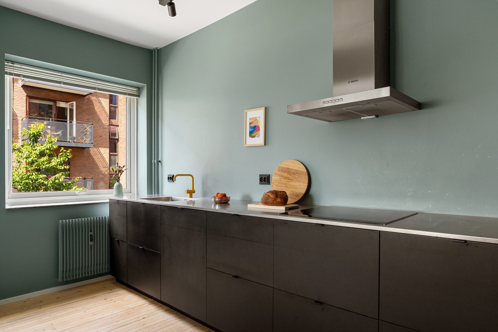 Kjøkkeninnredningen er utstyrt med sorte, glatte fronter og benkeplate i rustfritt stål med heldekkende benkebeslag. Galleribilde