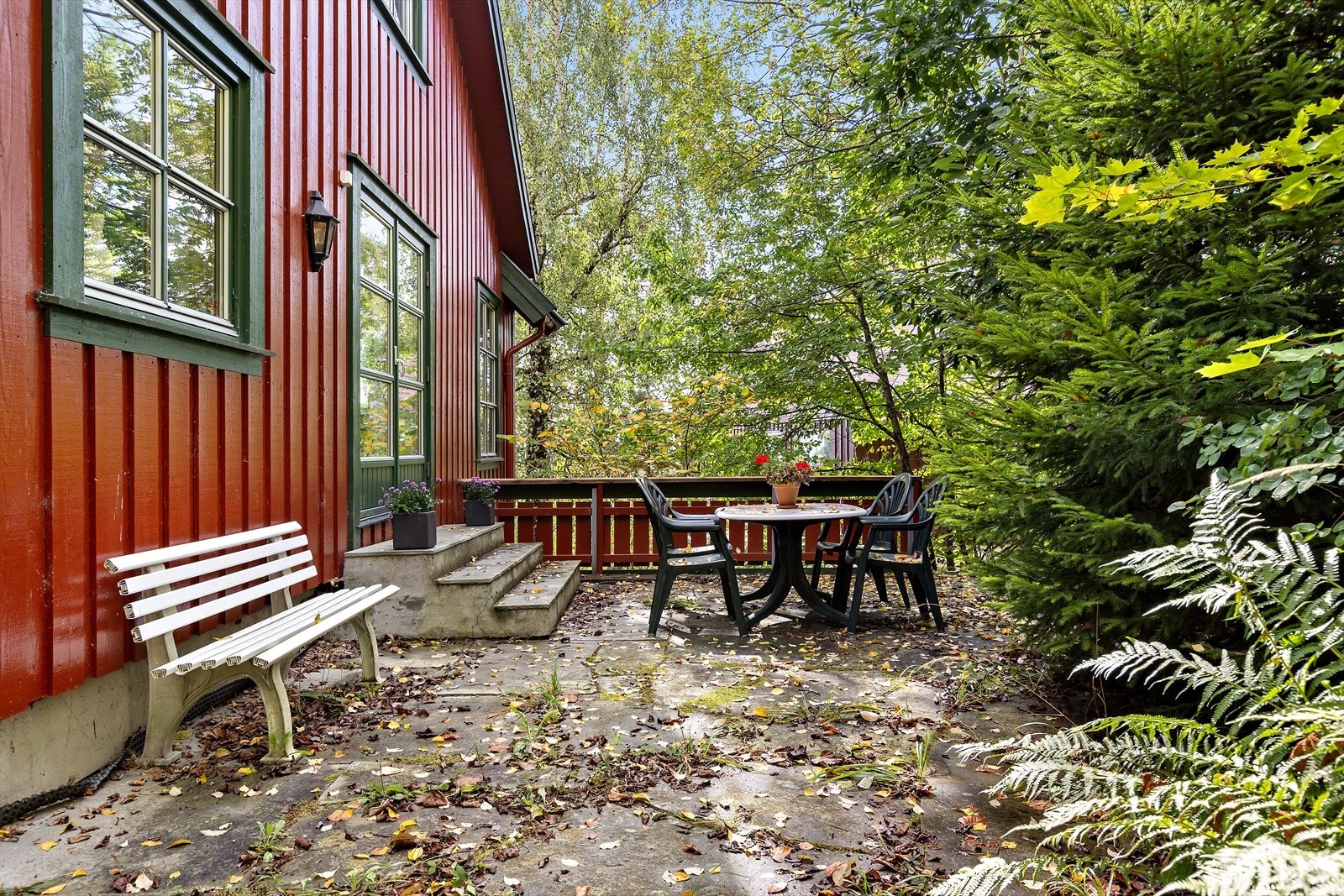 Fra spisestuen er det utgang til en stor, skiferlagt terrasse, skjermet av frodige løvtrær Galleribilde