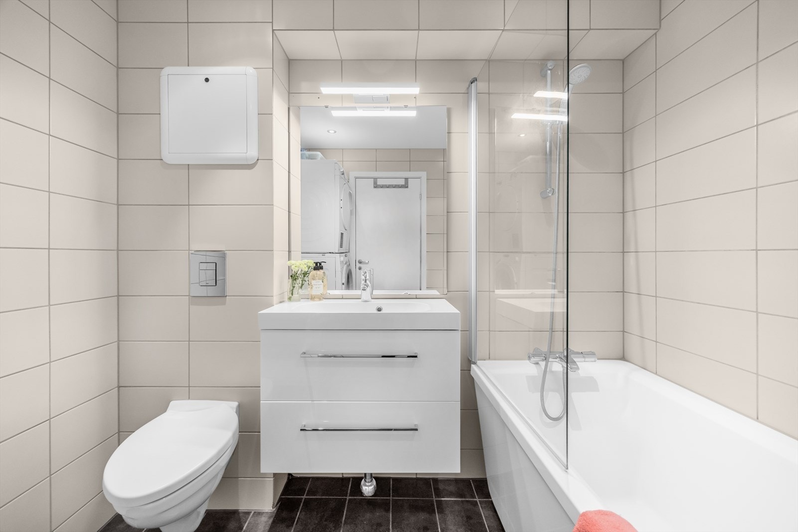 Badet er innredet med vegghengt klosett, baderomsinnredning med heldekkende servant, speil og badekar med dusjvegg. Galleribilde