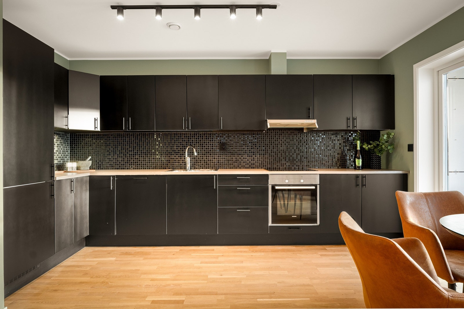 Moderne innredning med sorte glatte fronter, laminat benkeplate og fliser på vegg over benk. Integrert keramisk topp med komfyrvakt, stekeovn, oppvaskmaskin, frys og kjøleskap Galleribilde