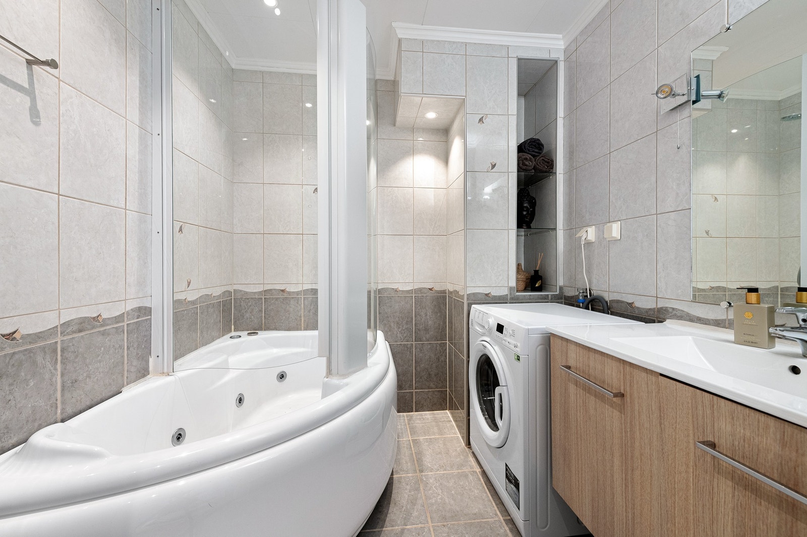 Flislagt bad med boblekar med dusjløsning, baderomsinnredning og opplegg for vaskemaskin. Galleribilde