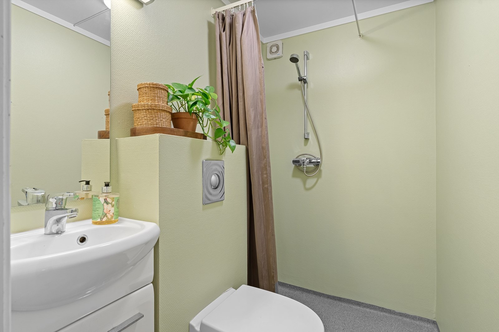 Badet har belegg på gulv med varmekabler, ellers malte overflater. Det inneholder et vegghengt toalett, dusj med forheng, samt baderomsinnredning med speil og belysning over. Ny himling her i 2025. Galleribilde