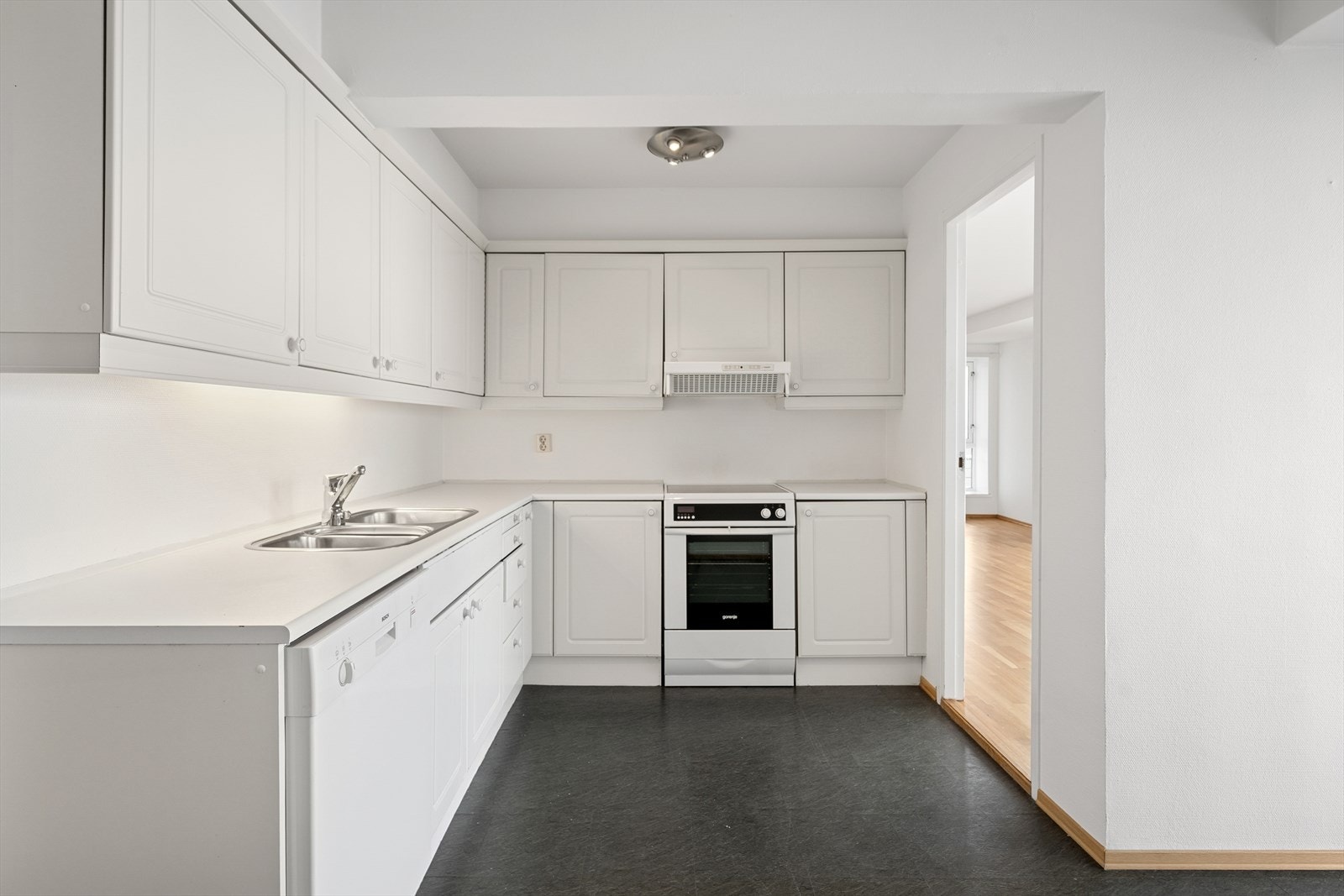 Adskilt kjøkkenløsning med innredning fra byggeår. Innredningen har profilerte fronter, benkeplate i laminat og belysning under overskap. Galleribilde