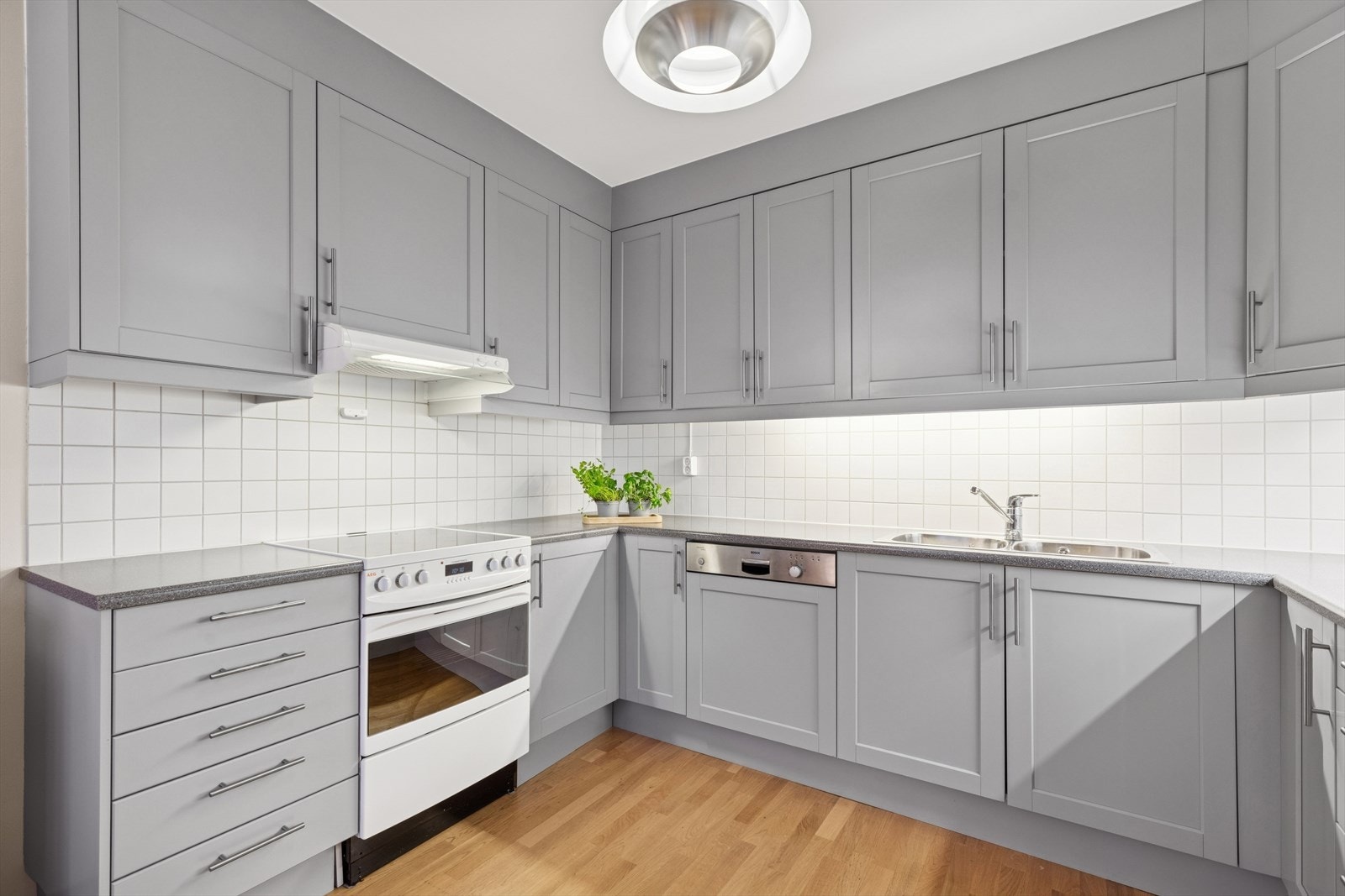 Kjøkkenet er stilrent, med enkle speilprofiler på skapfronter. Det er rikelig utstyrt med skap-, skuff-, og benkeplass. Fliser mellom kjøkkenbenk og overskap er både dekorativt og praktisk mtp daglig renhold. Galleribilde