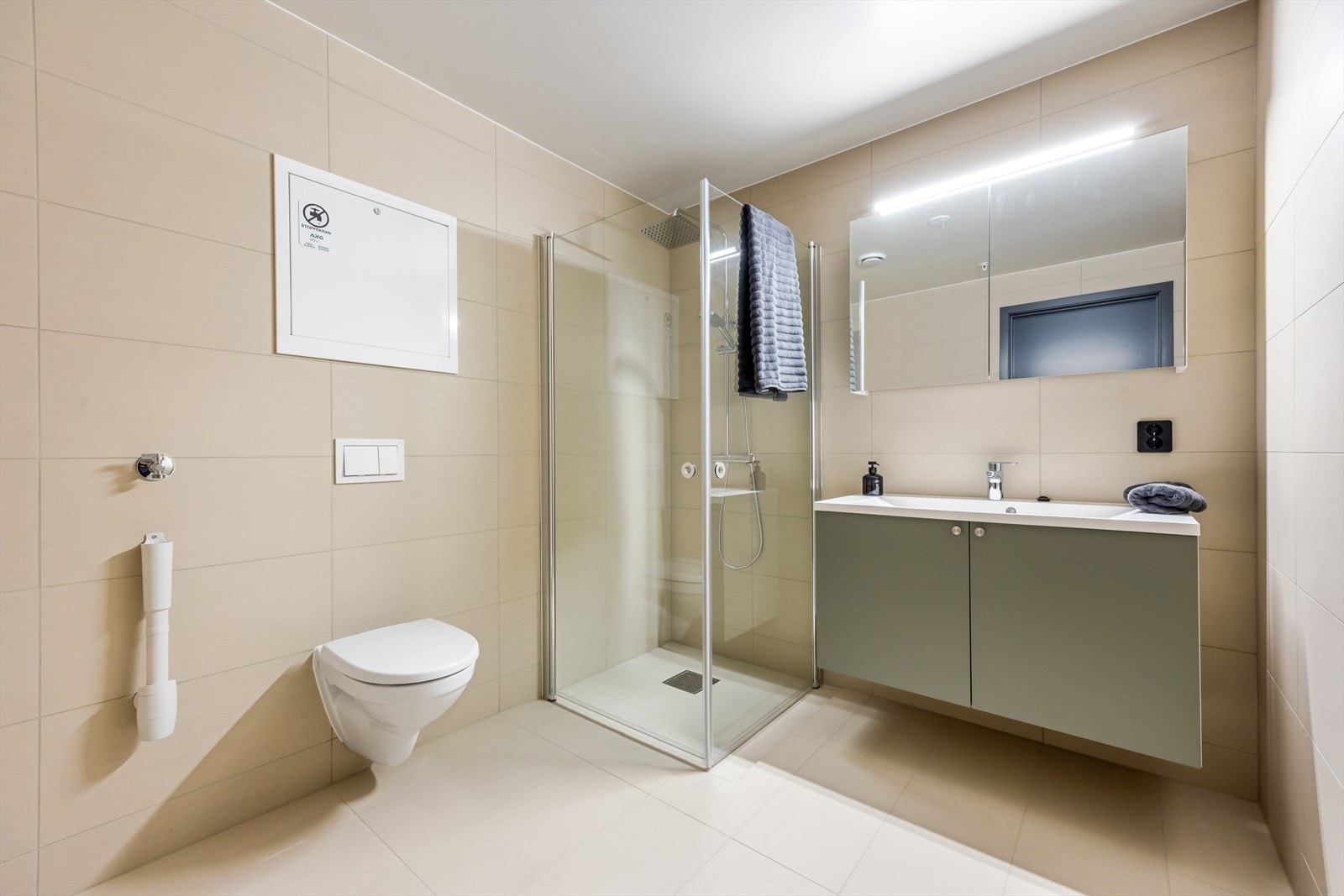 Delikat baderom med store fliser i en lys, matt beige farge. Baderomsinnredning fra Sigdal i vakker blågrønn farge. Galleribilde