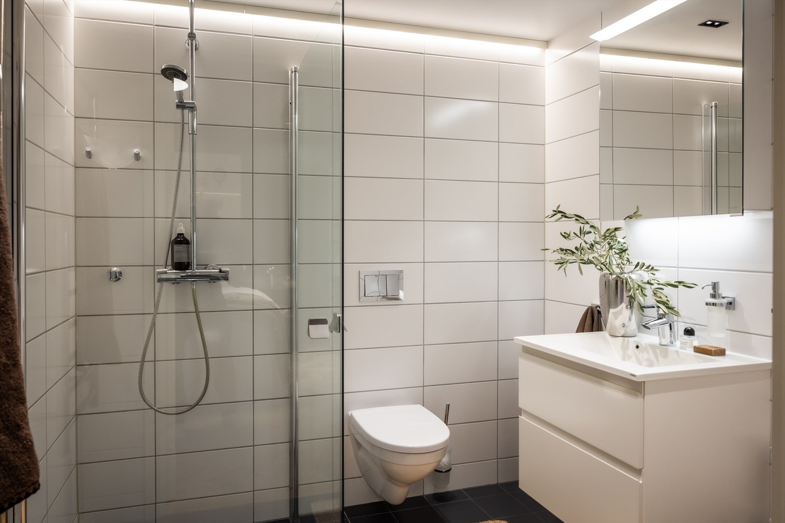 Flislagt bad med dusjhjørne med INR dusjvegger samt vegghengt skuffeinnredning med hvite glatte fronter og heldekkende servant benkeplate. Galleribilde