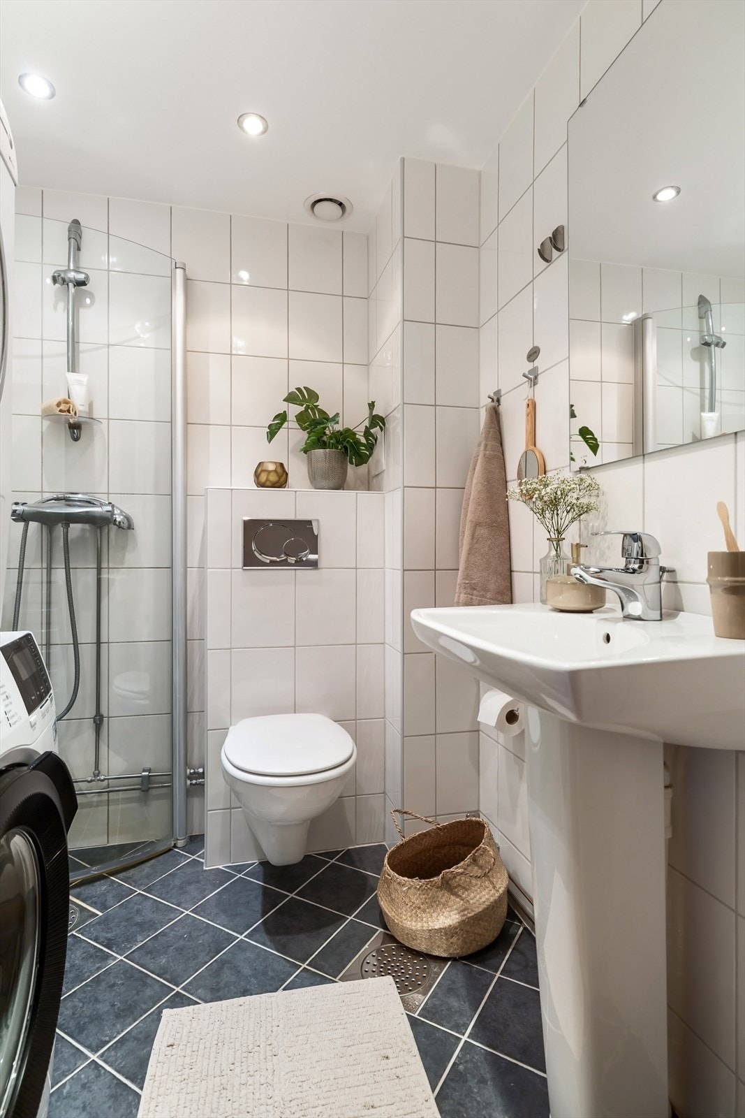 Badet inneholder vegghengt servant med ett-greps blandebatteri, speil på vegg, dusjhjørne med glassdører og vegghengt toalett. Galleribilde