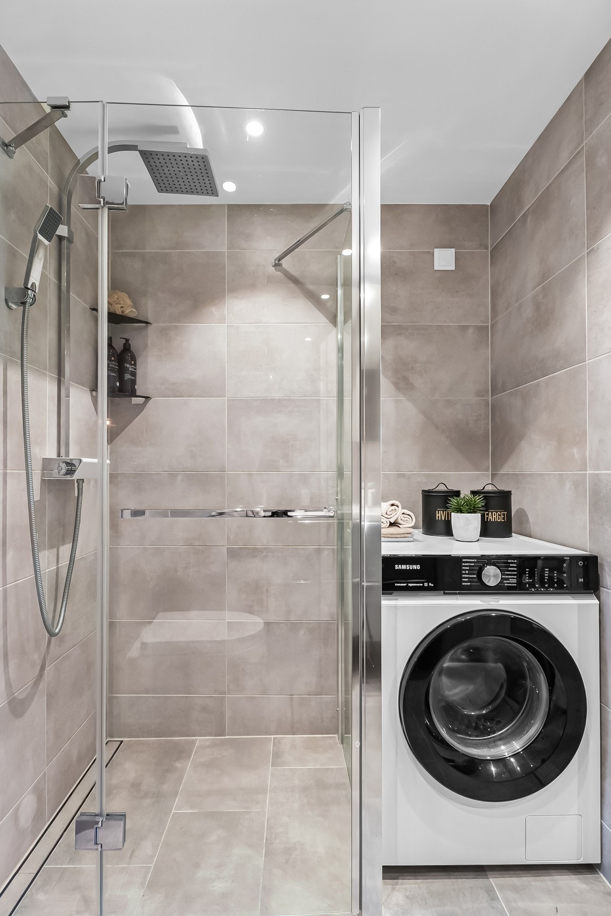 Badet er utstyrt med veggmontert klosett og opplegg for vaskemaskin. Eget dusjhjørne, med svingdører i glass, rennesluk, regnfallsdusj og termostatstyrt blandebatteri. Galleribilde